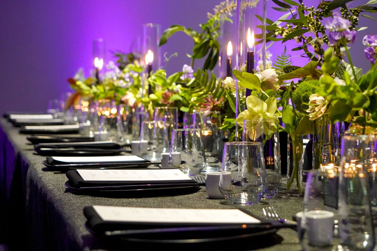 Long dining table with green floral centerpieces and formal place settings.