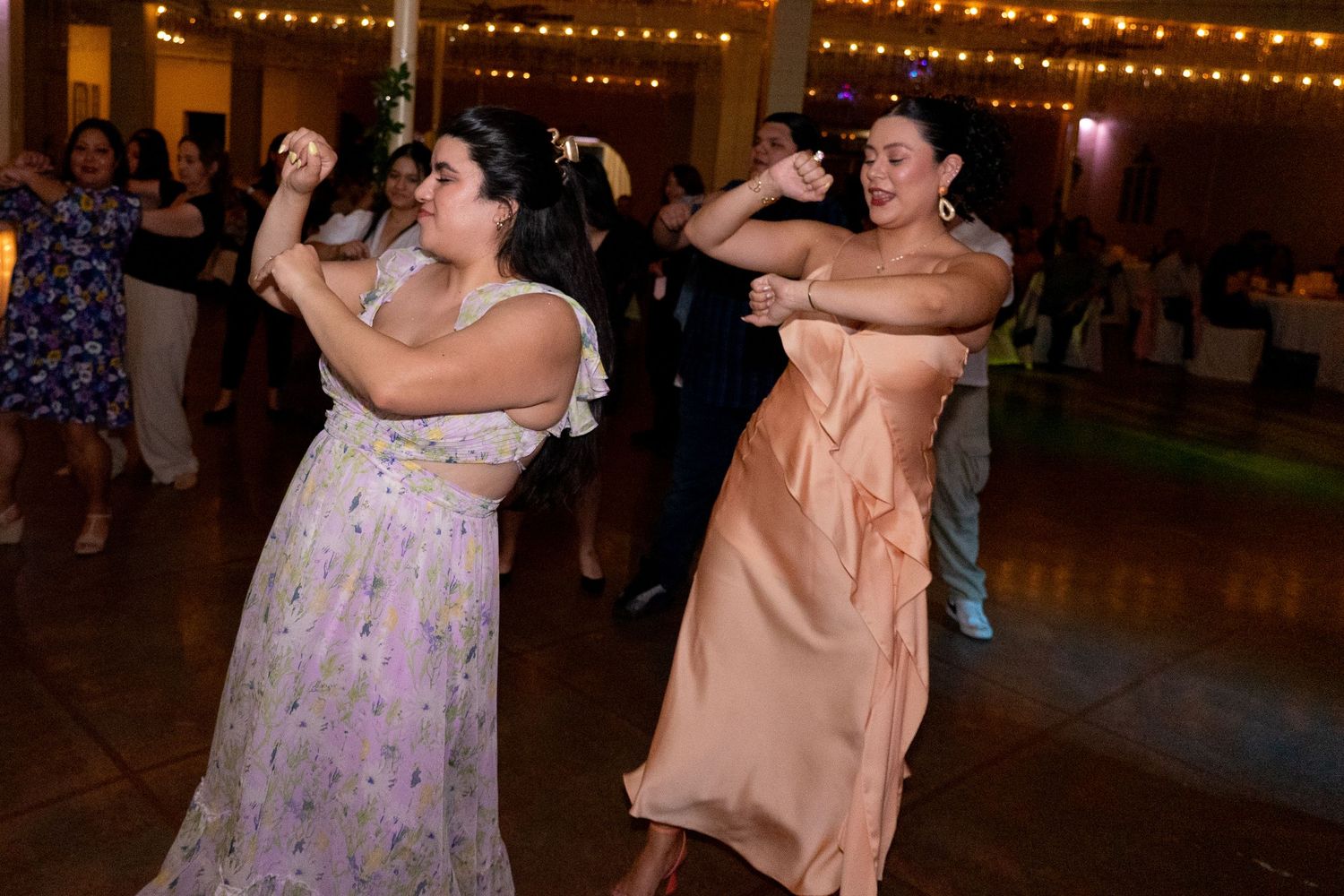 Couples dancing together under warm string lights at an evening celebration.