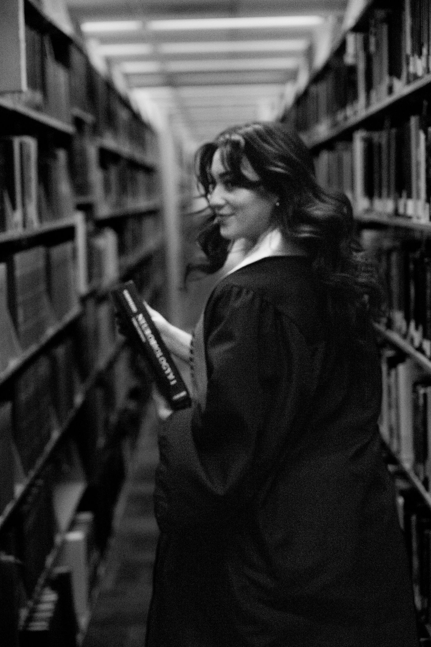 Artistic black and white photos of graduate in library stacks.