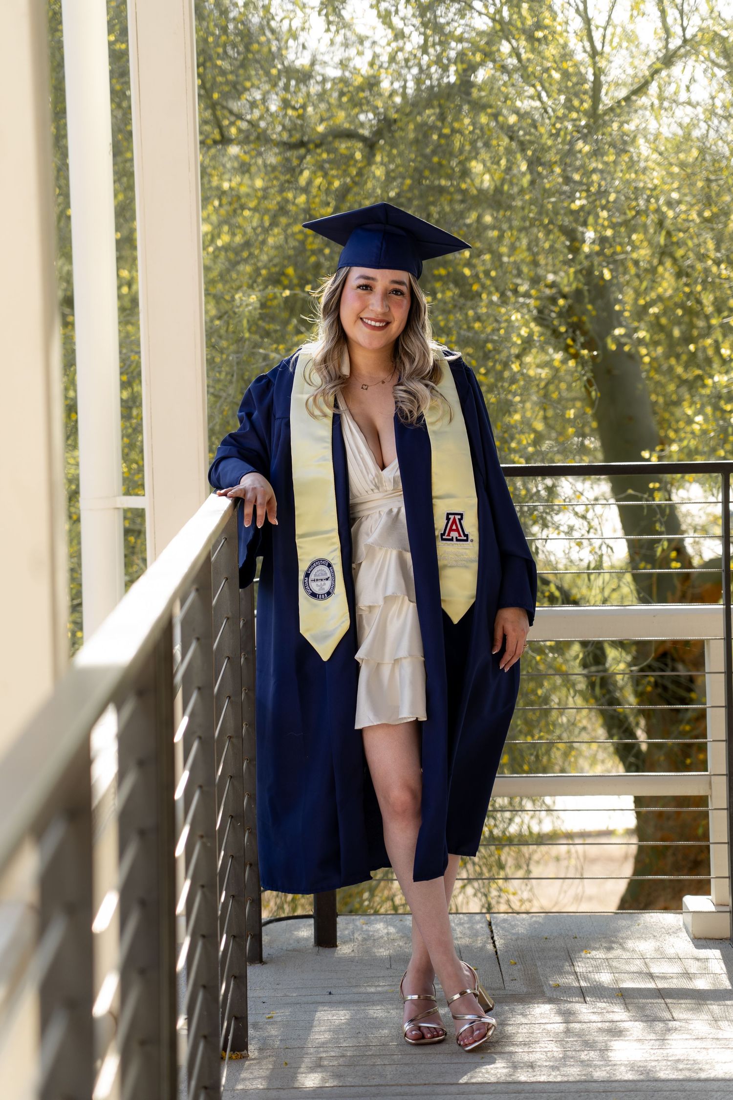 Graduate in navy blue cap and gown poses on Old Main porch at the University of Arizona.