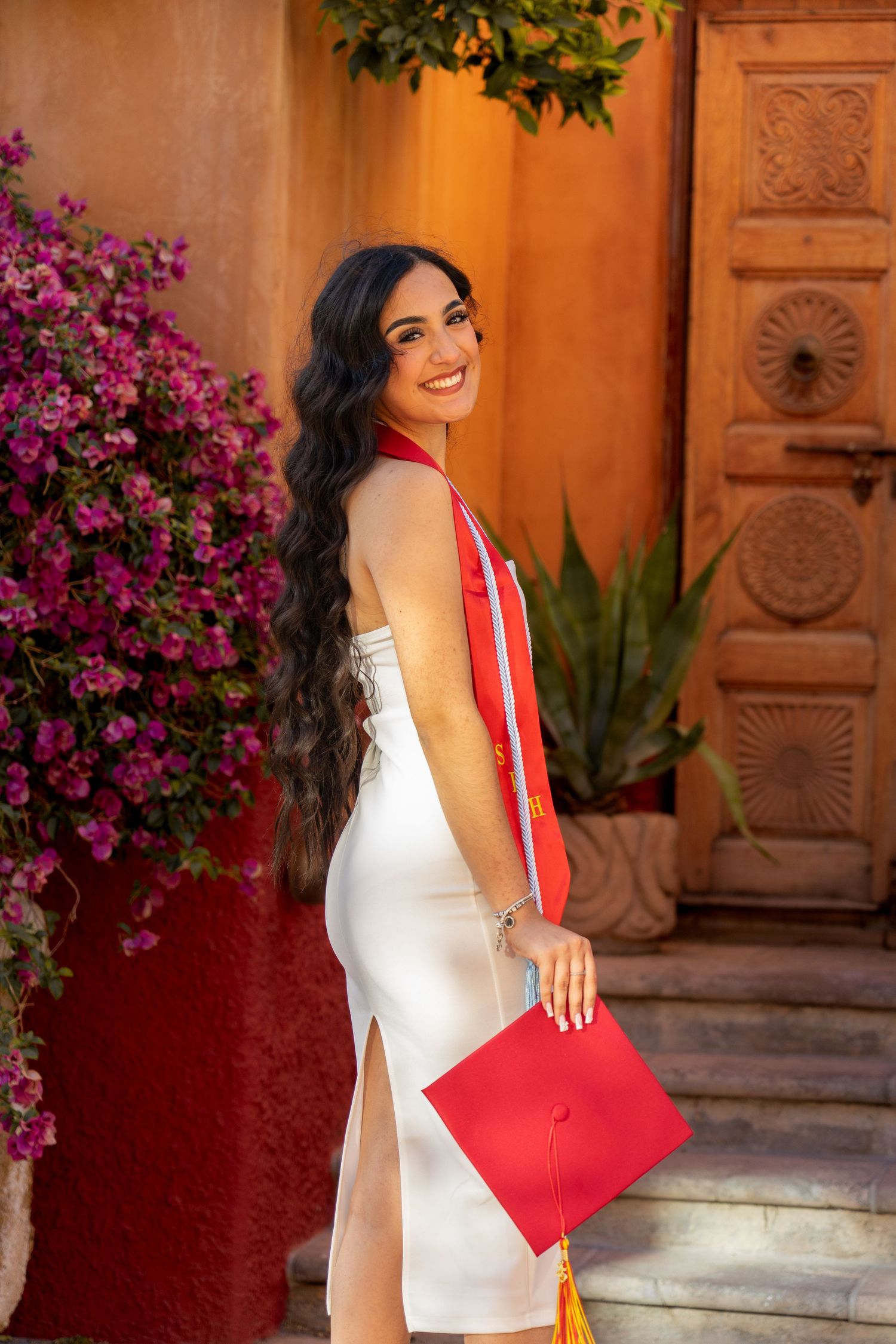 White dress graduation photos with red diploma holder against floral backdrop.