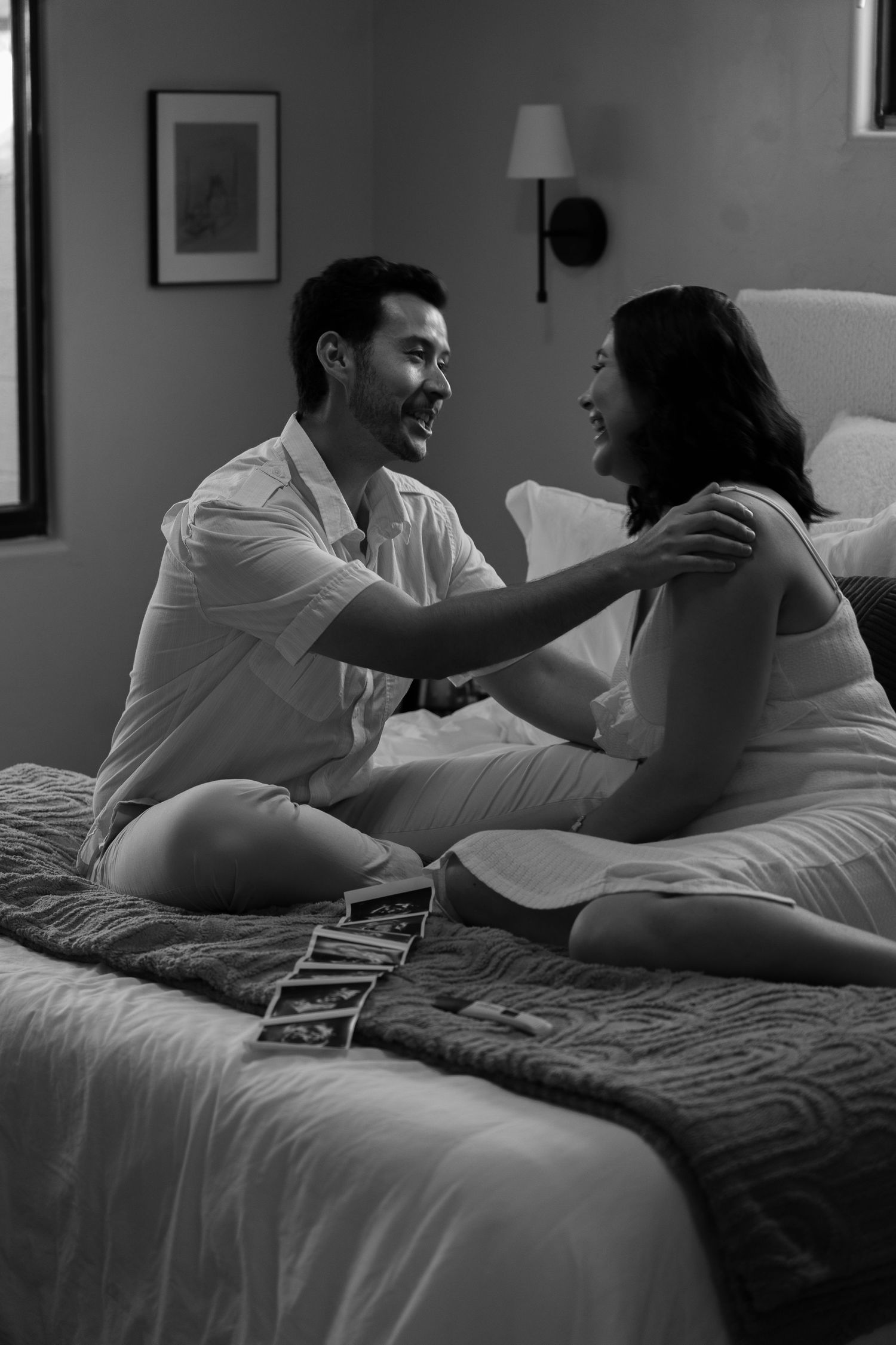 Couple sharing joyful moment on bed with ultrasound photos displayed.