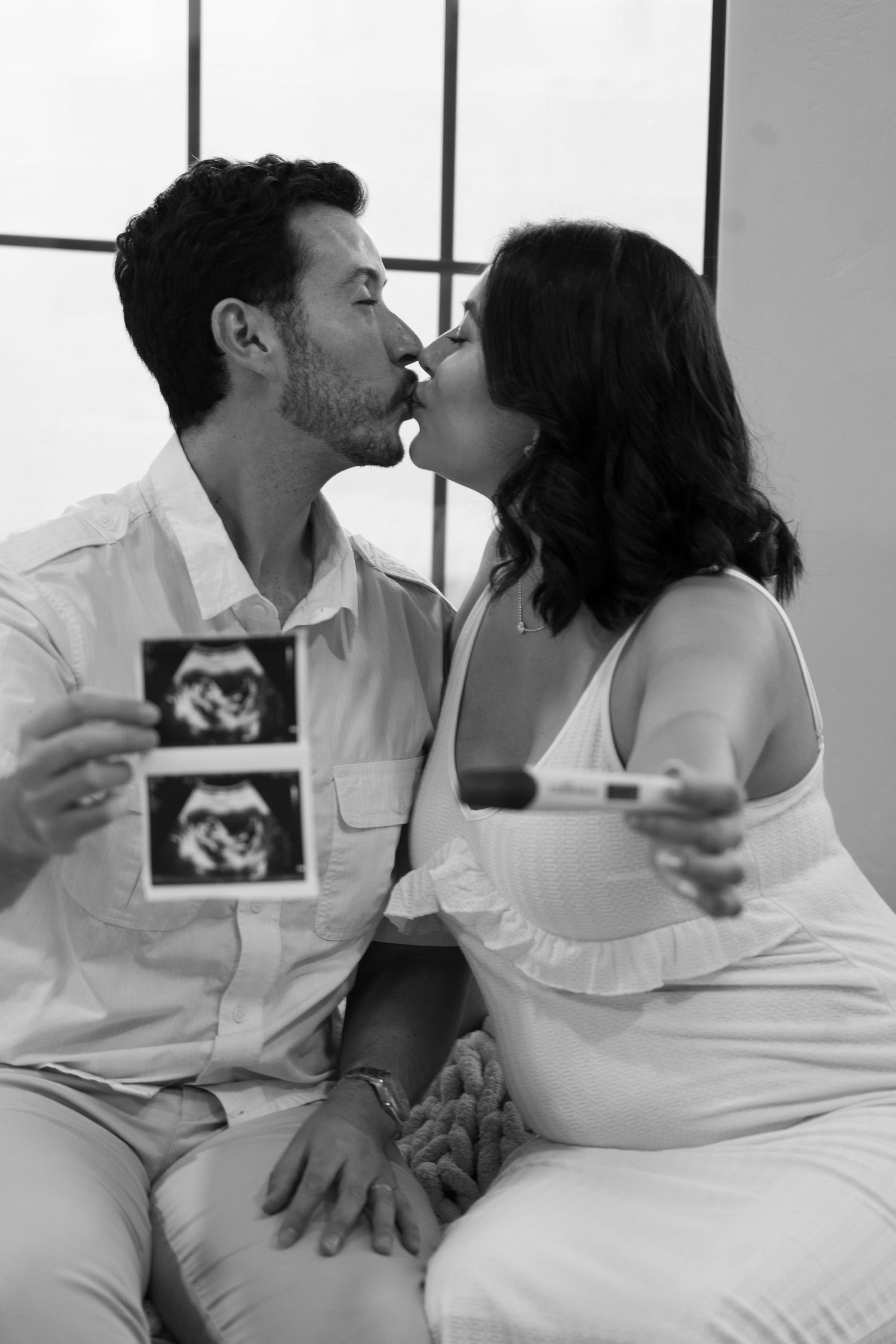 Couple sharing tender moment while holding ultrasound photo during pregnancy announcement shoot.
