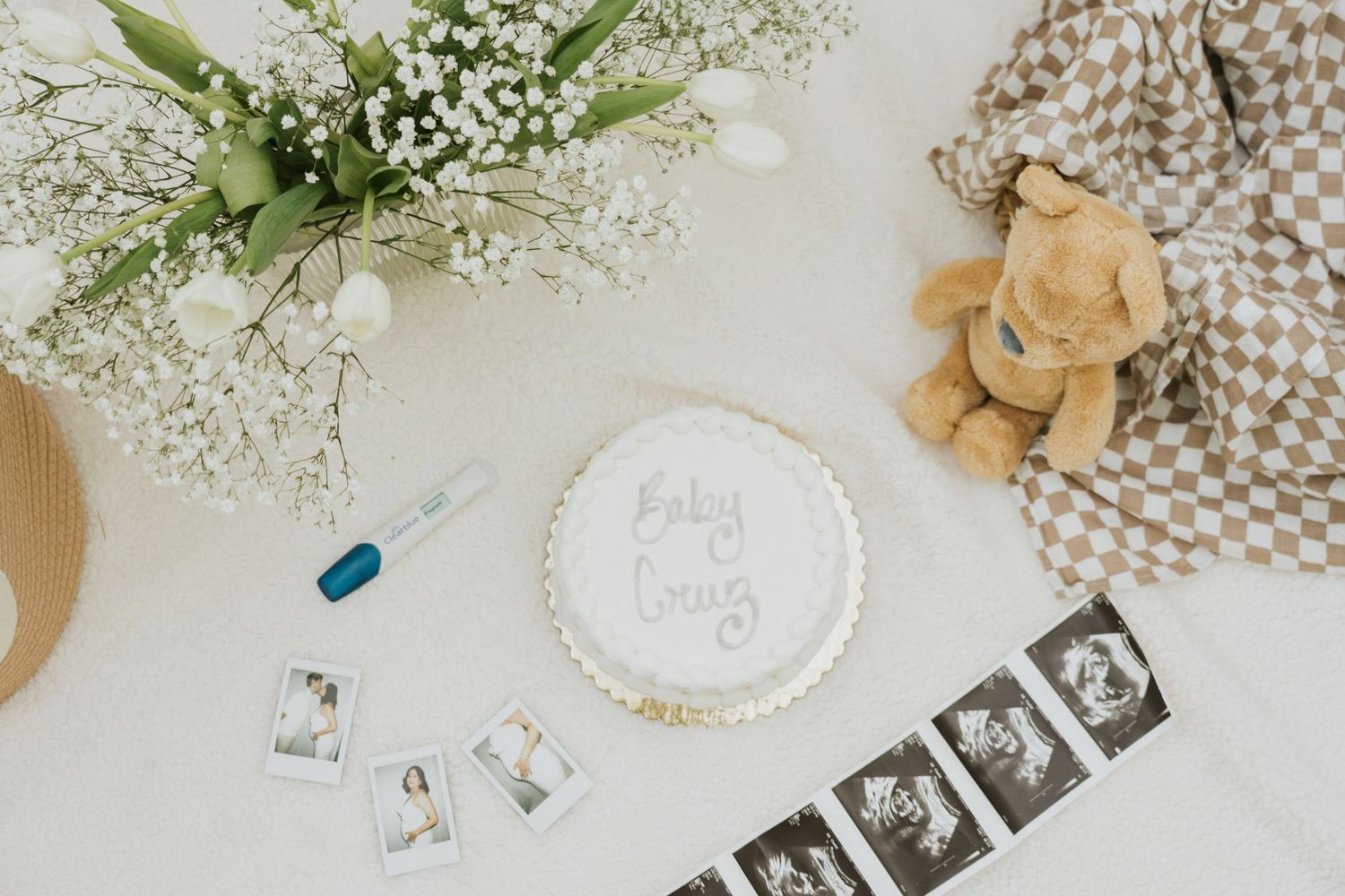 Maternity photoshoot display with sonogram images, teddy bear, and baby's breath flowers arranged on white fabric.