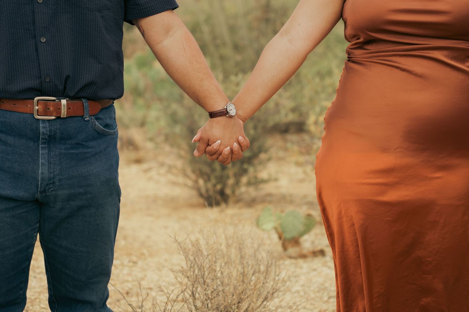 Close-up of couple's hands holding each other in a desert landscape.