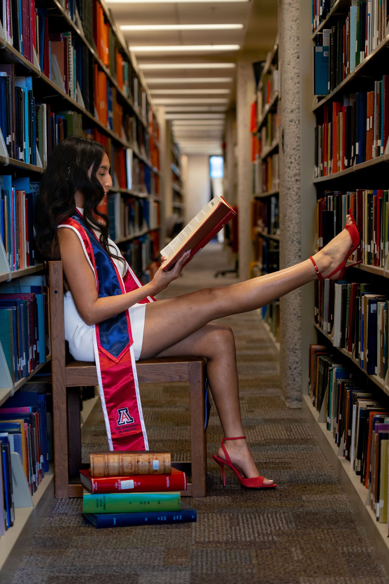 Creative graduation photo shoot in library with books and academic regalia.