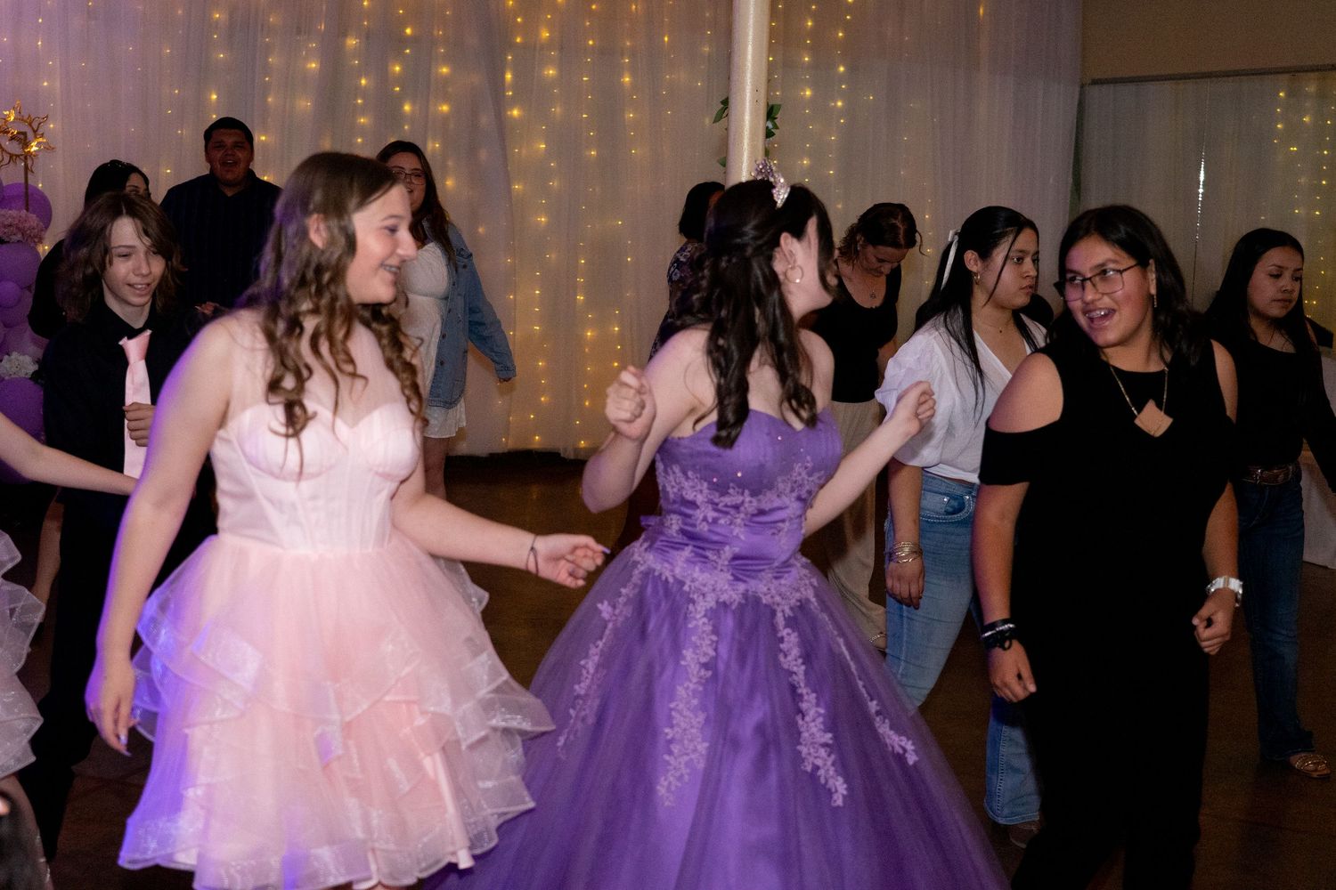 Dancers in purple and pink formal dresses twirling on a ballroom dance floor.
