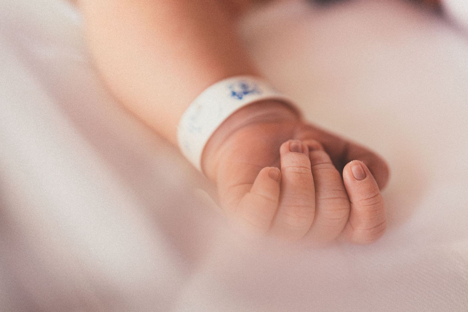 Close-up of a newborn baby hand with a hospital identification bracelet resting on a white blanket.
