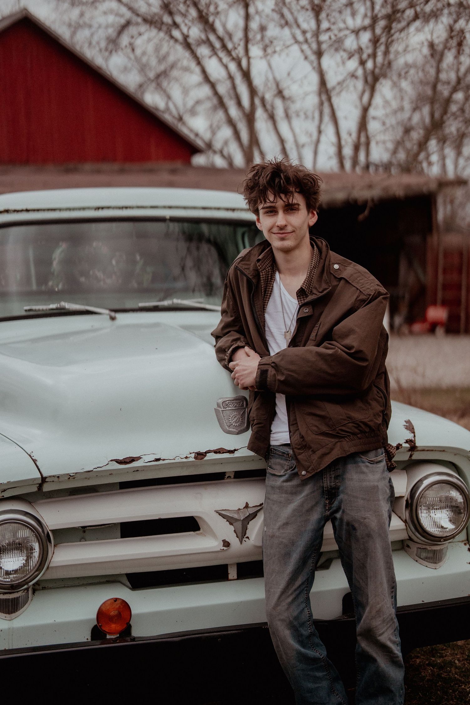 Moody photography session with vintage car and red barn in winter setting.