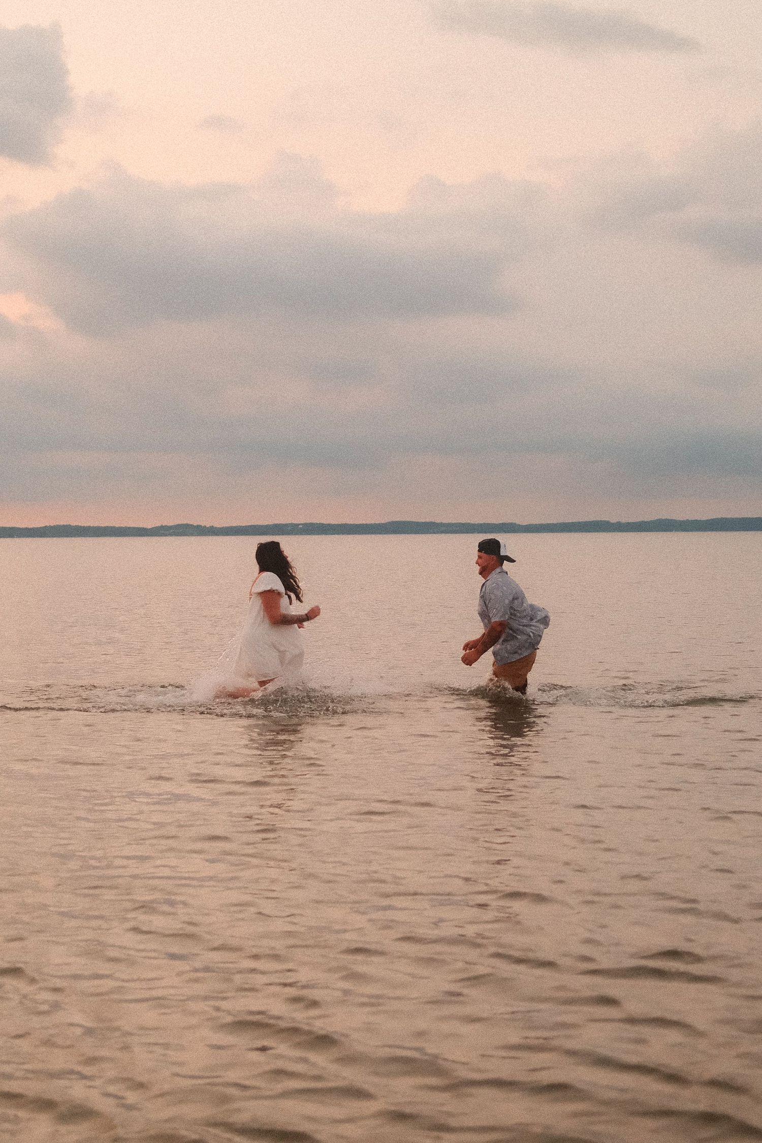 Two figures splashing in shallow water at sunset on a tranquil lake.