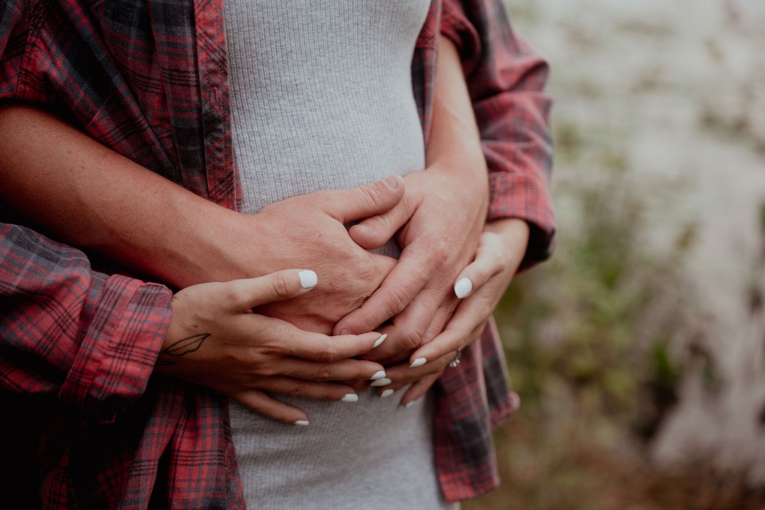 Close-up shots of hands tenderly embracing in casual outdoor setting.