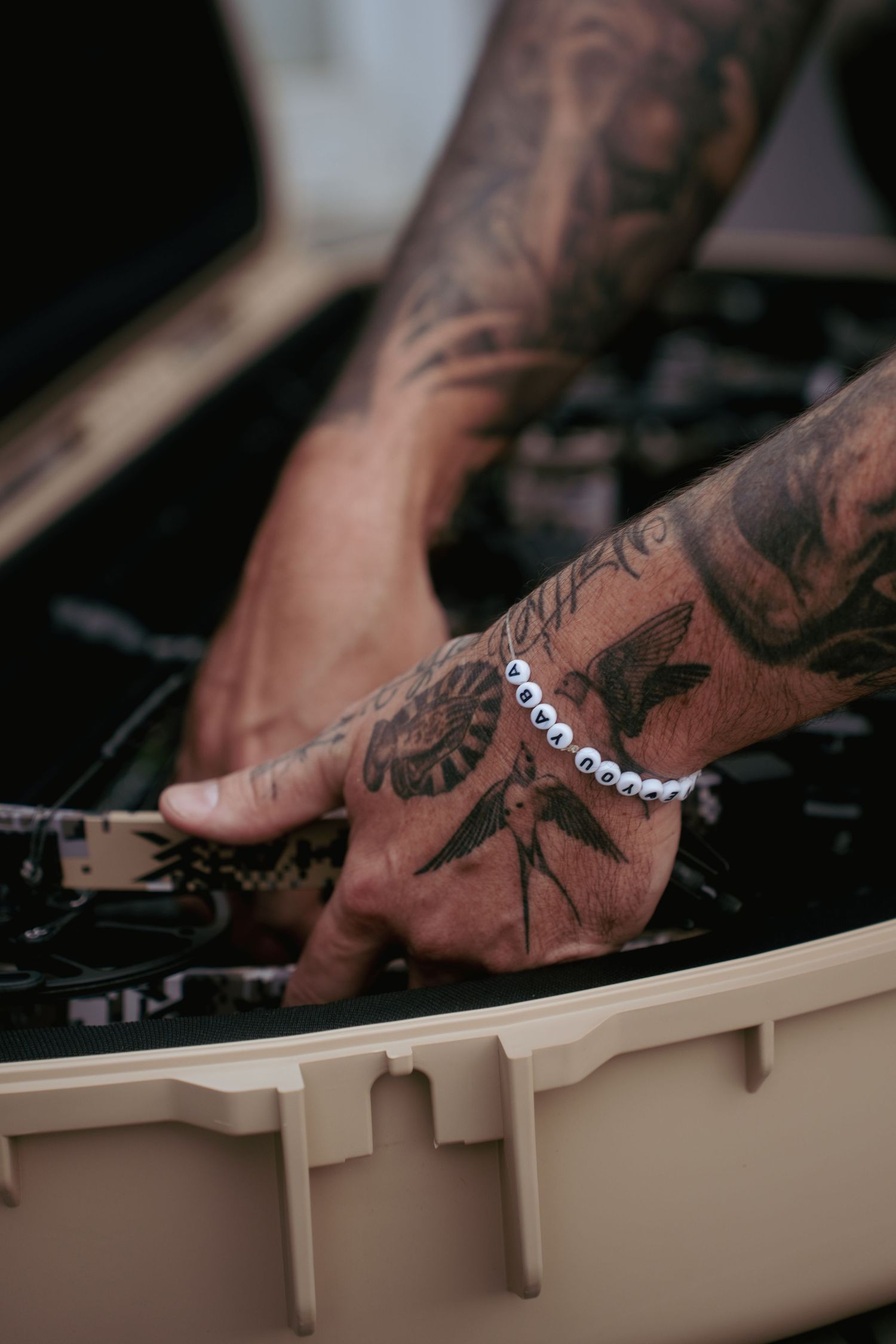 Tattooed hands with intricate designs working on beige equipment or machinery.