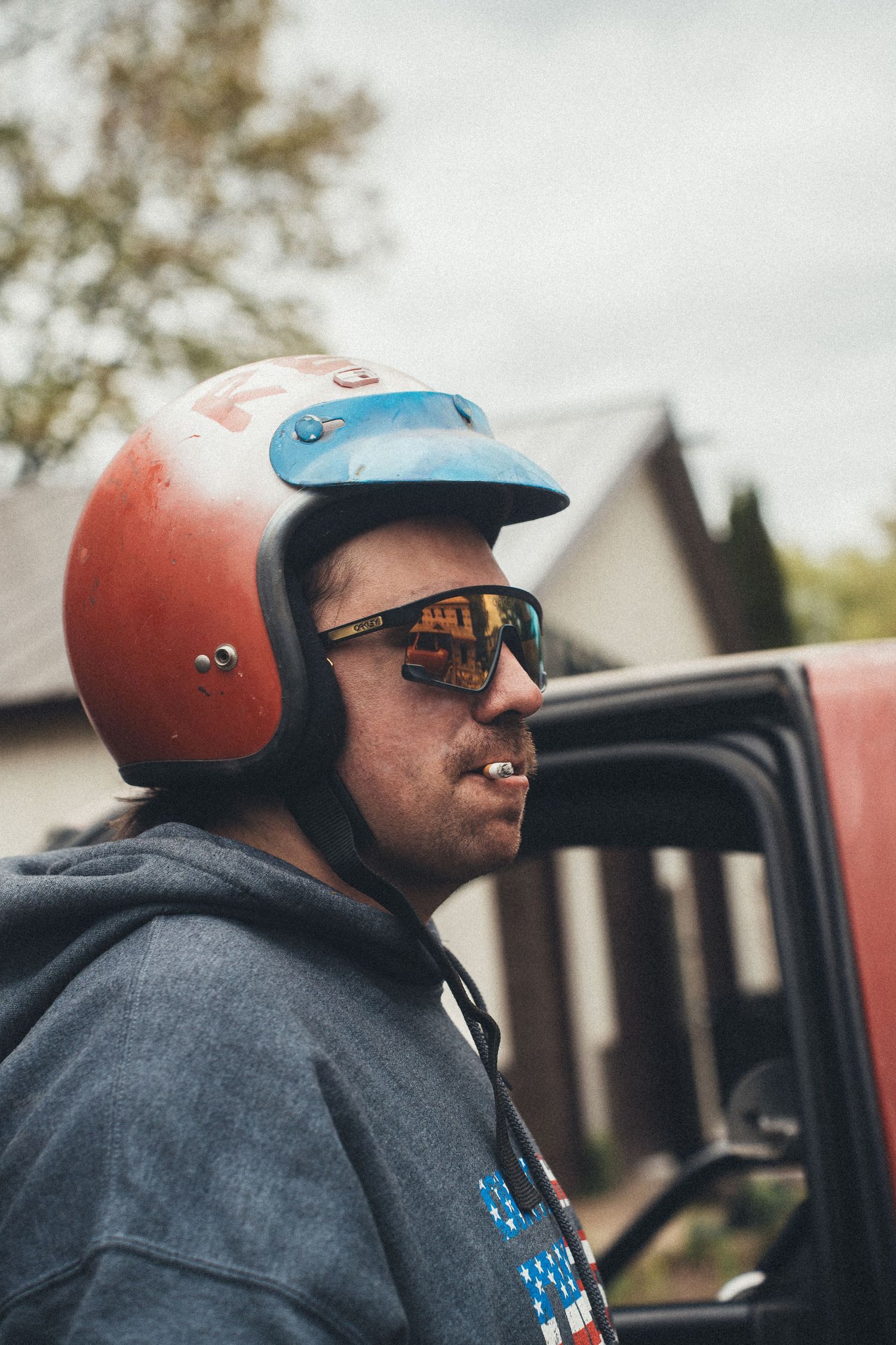 Person in a gray hoodie wearing an orange helmet and sunglasses shown from different angles while seated.