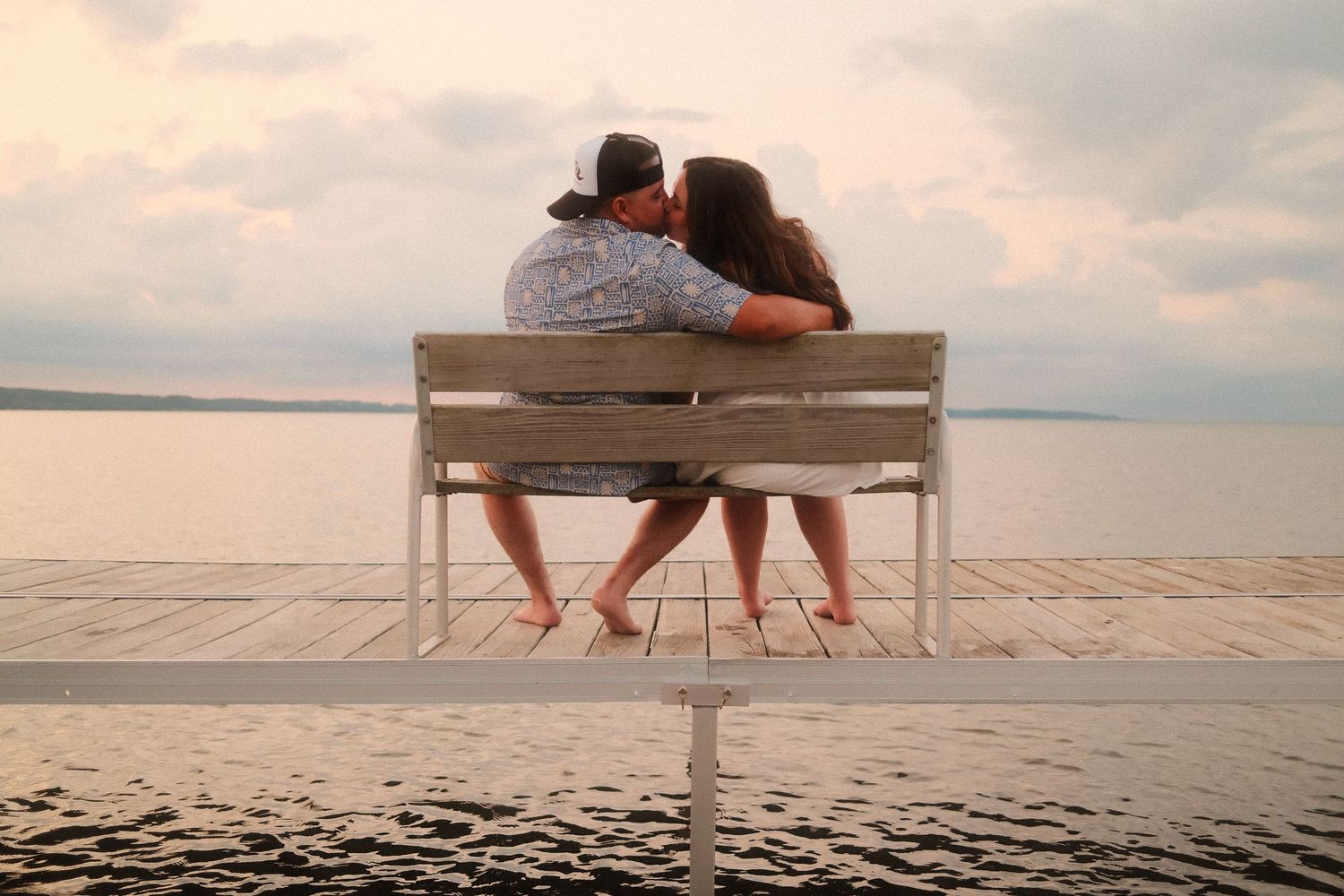 Couple sitting on wooden bench overlooking a serene waterfront at sunset.