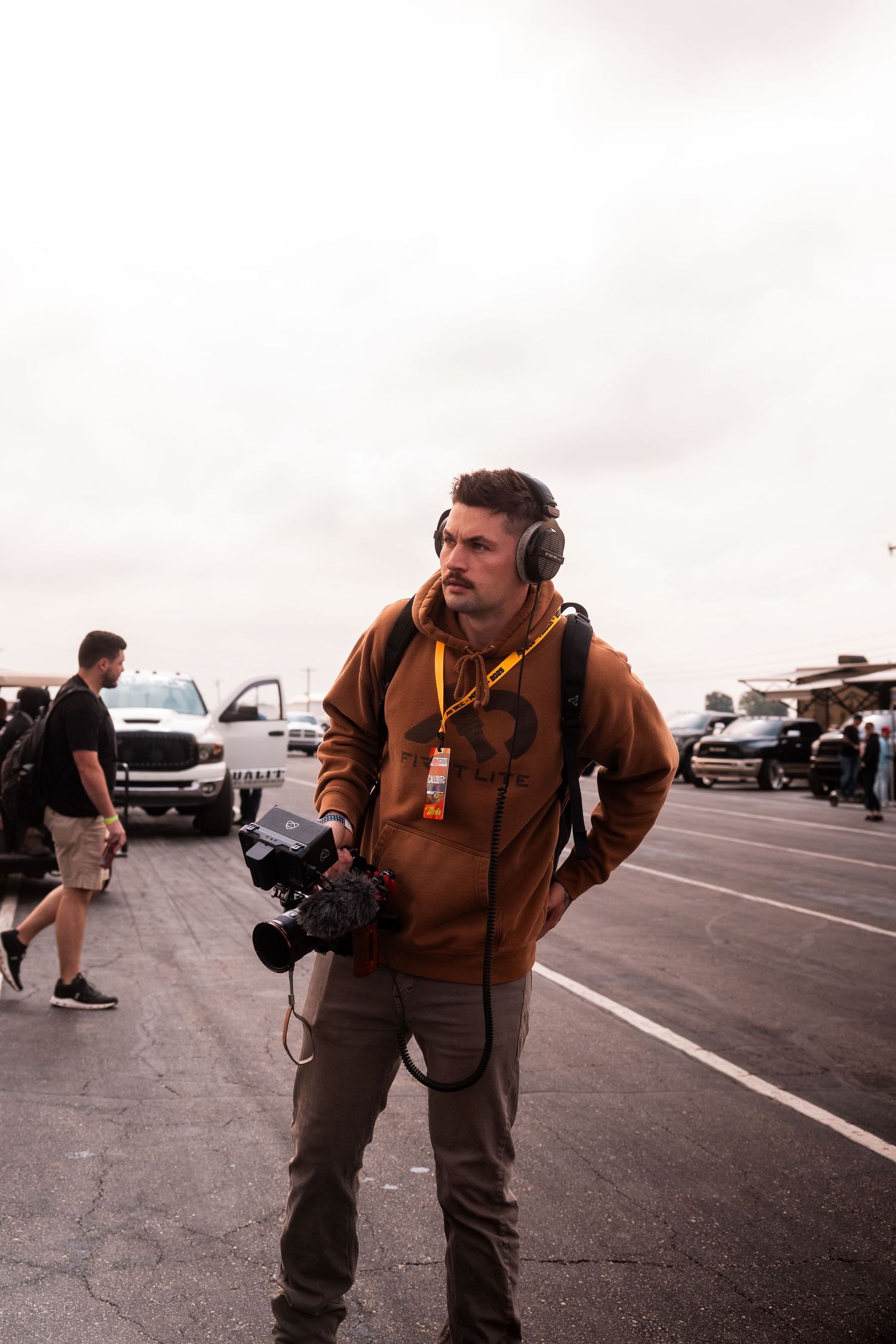 Photographer with camera and headphones stands in parking lot on overcast day.