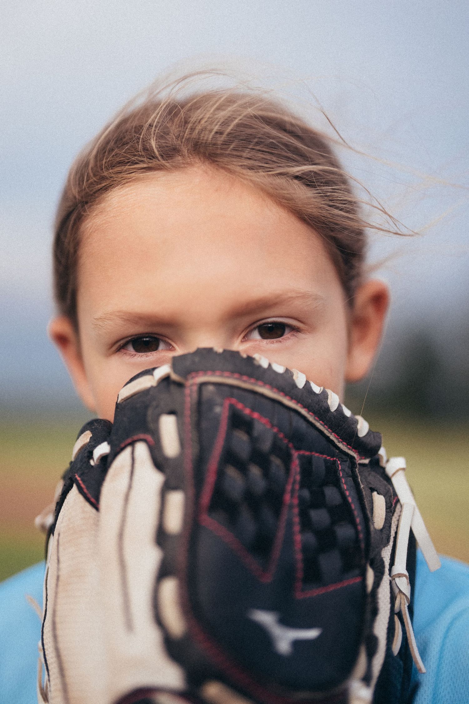 Young girl holding a Mizuno baseball glove up to her face outdoors on a baseball field.