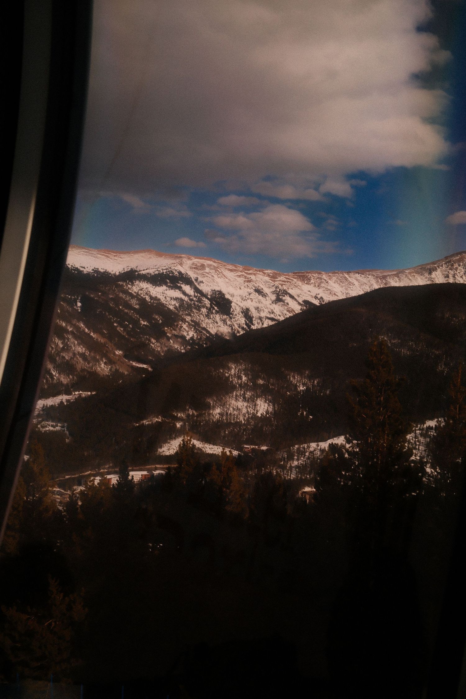 Dramatic mountain landscape with snow-covered peaks against a cloudy blue sky.