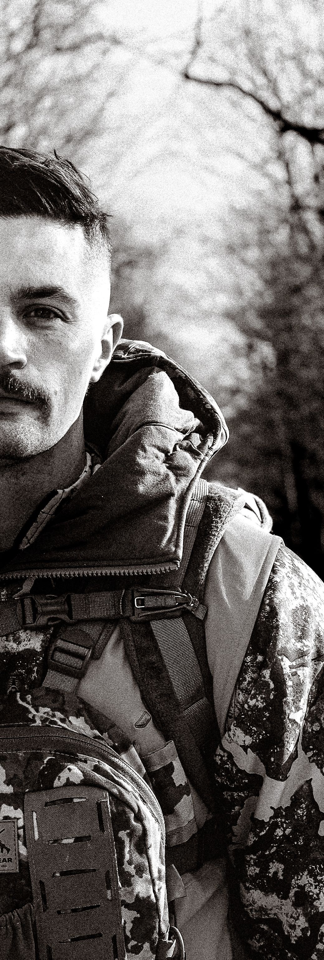 Black and white portrait of someone wearing tactical military gear with a backpack in an outdoor winter setting.