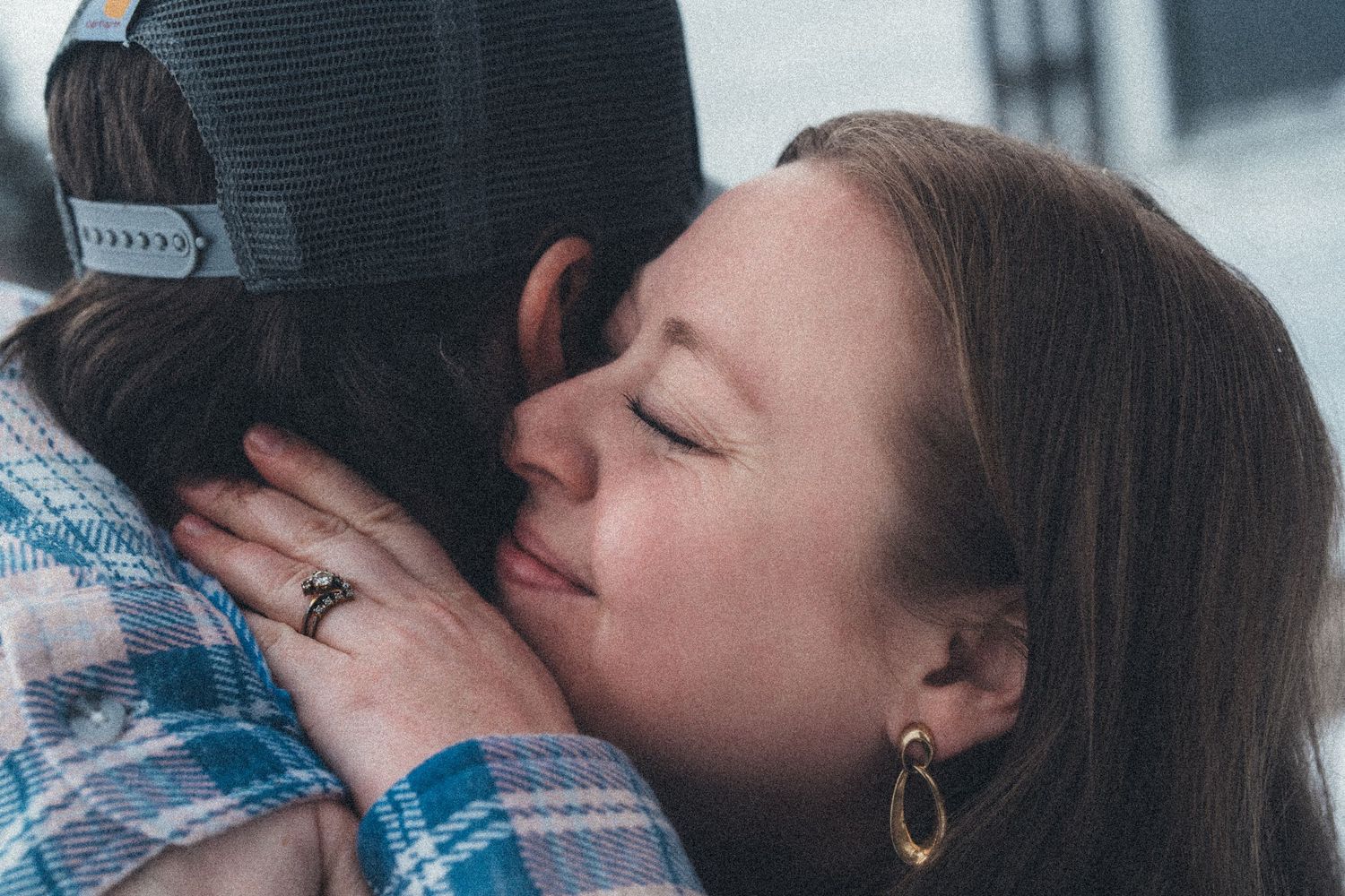 A couple shares a tender embrace and kiss while standing outdoors on a winter day.
