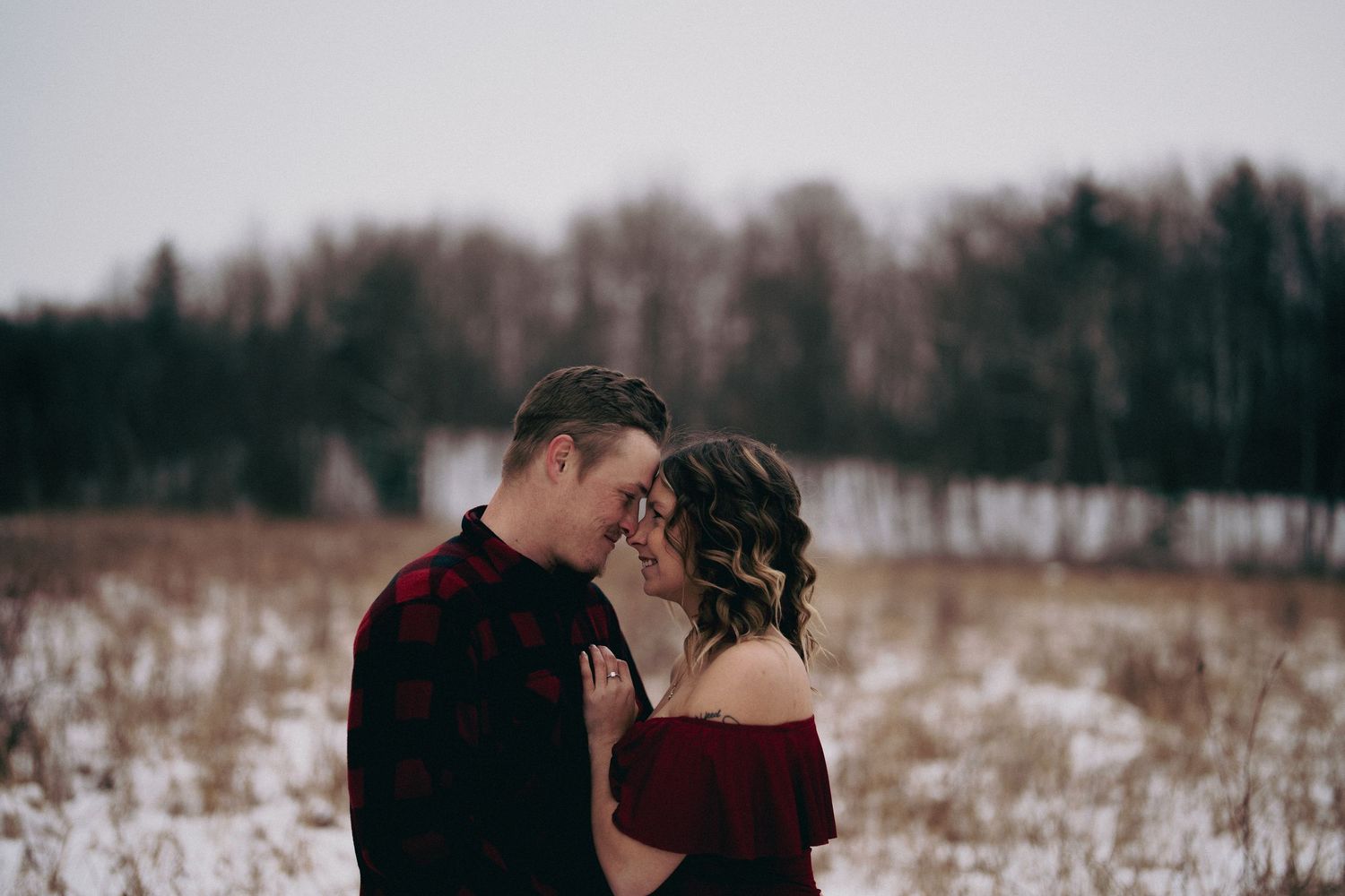 Couple embracing in a snowy winter landscape with trees in the background.