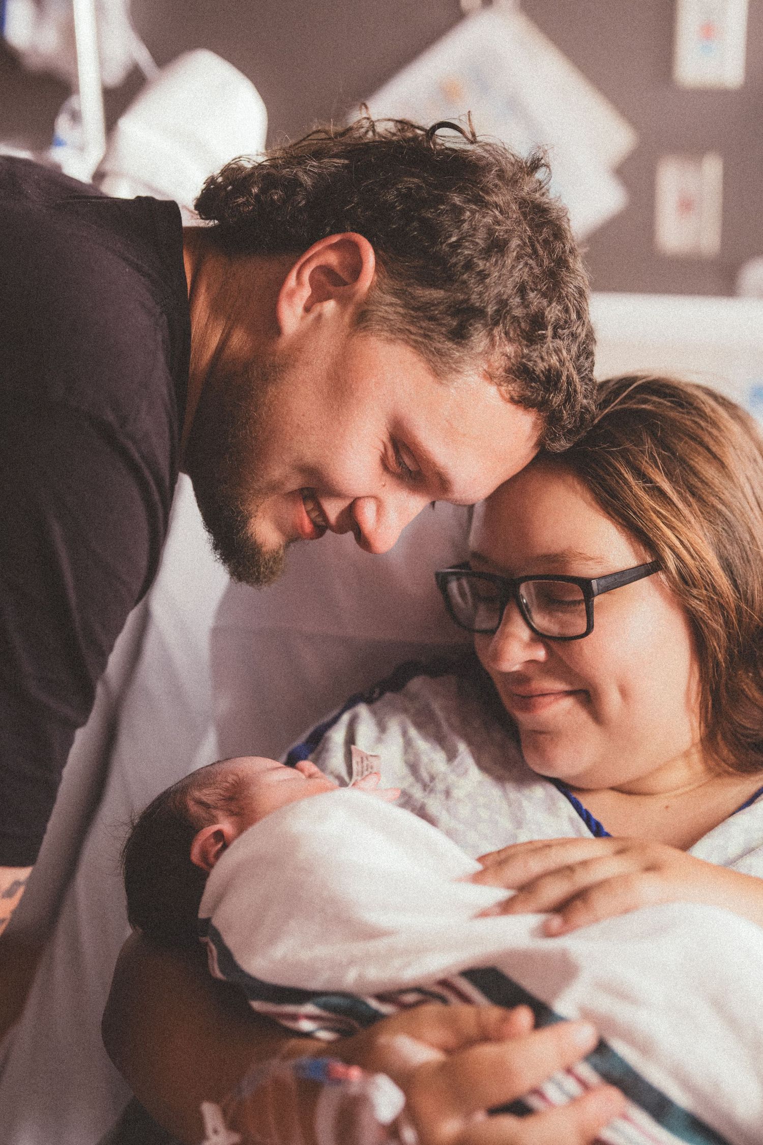 New parents lovingly gaze at their swaddled newborn baby in a hospital room after birth.