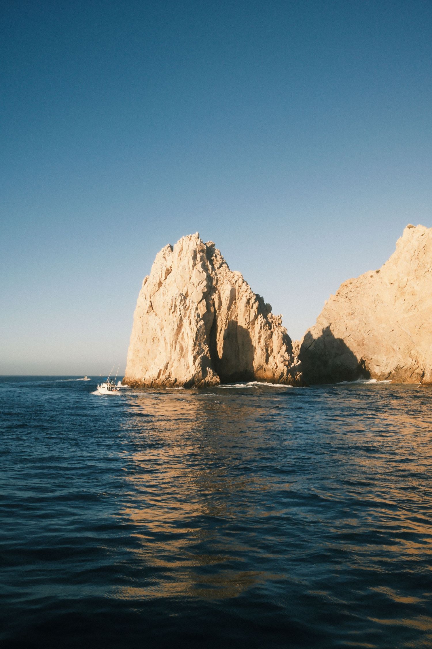 Dramatic rock formations at El Arco in Cabo San Lucas emerging from blue waters at sunset.