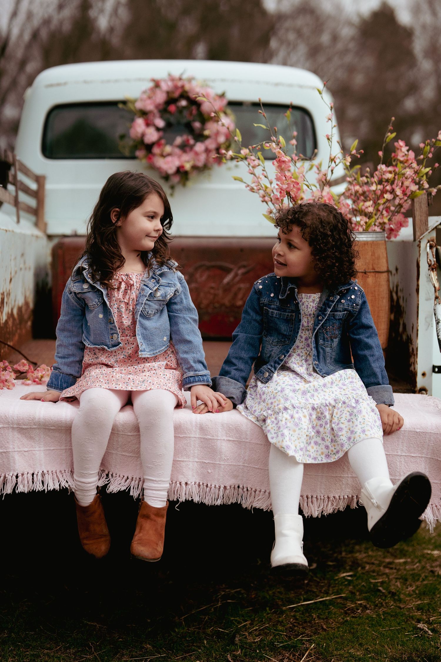 Children sitting on vintage truck bed with pink blanket and floral decorations.