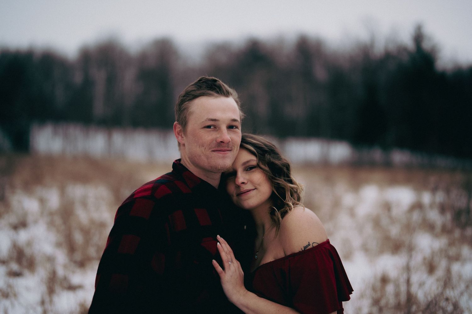Couple embracing in snowy winter field during portrait session.