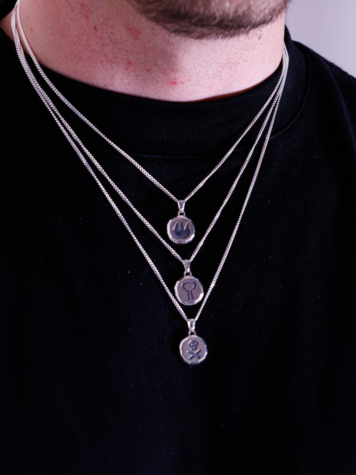 Man wearing three layered silver coin pendant necklaces over a black t-shirt.