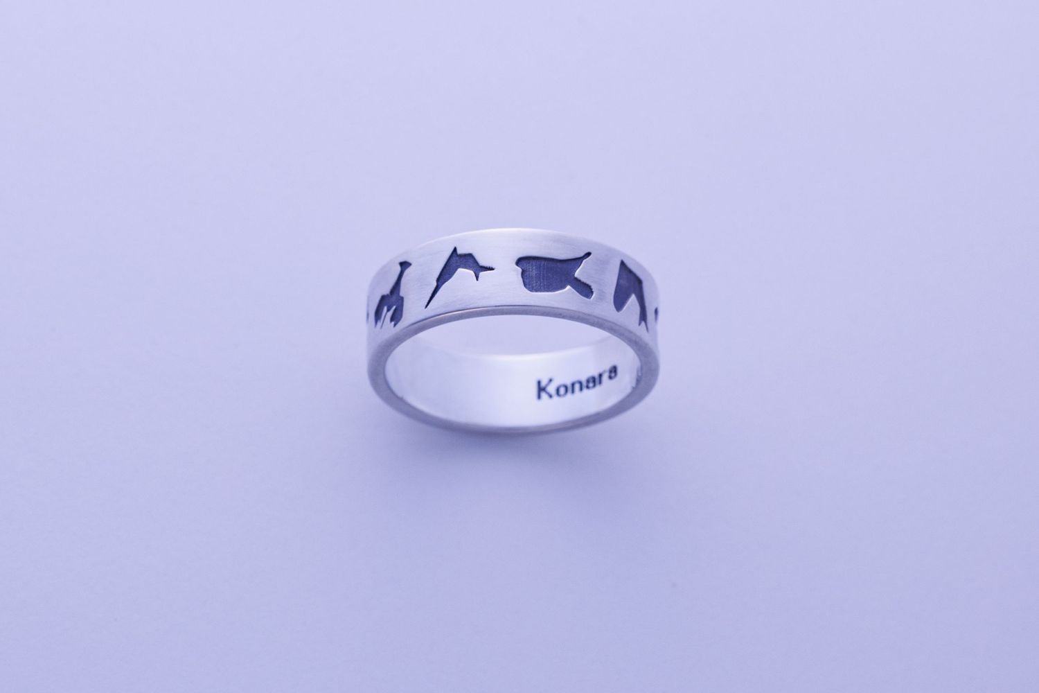 Silver band ring engraved with animal silhouettes including giraffe and dolphin, inscribed with Konara inside.