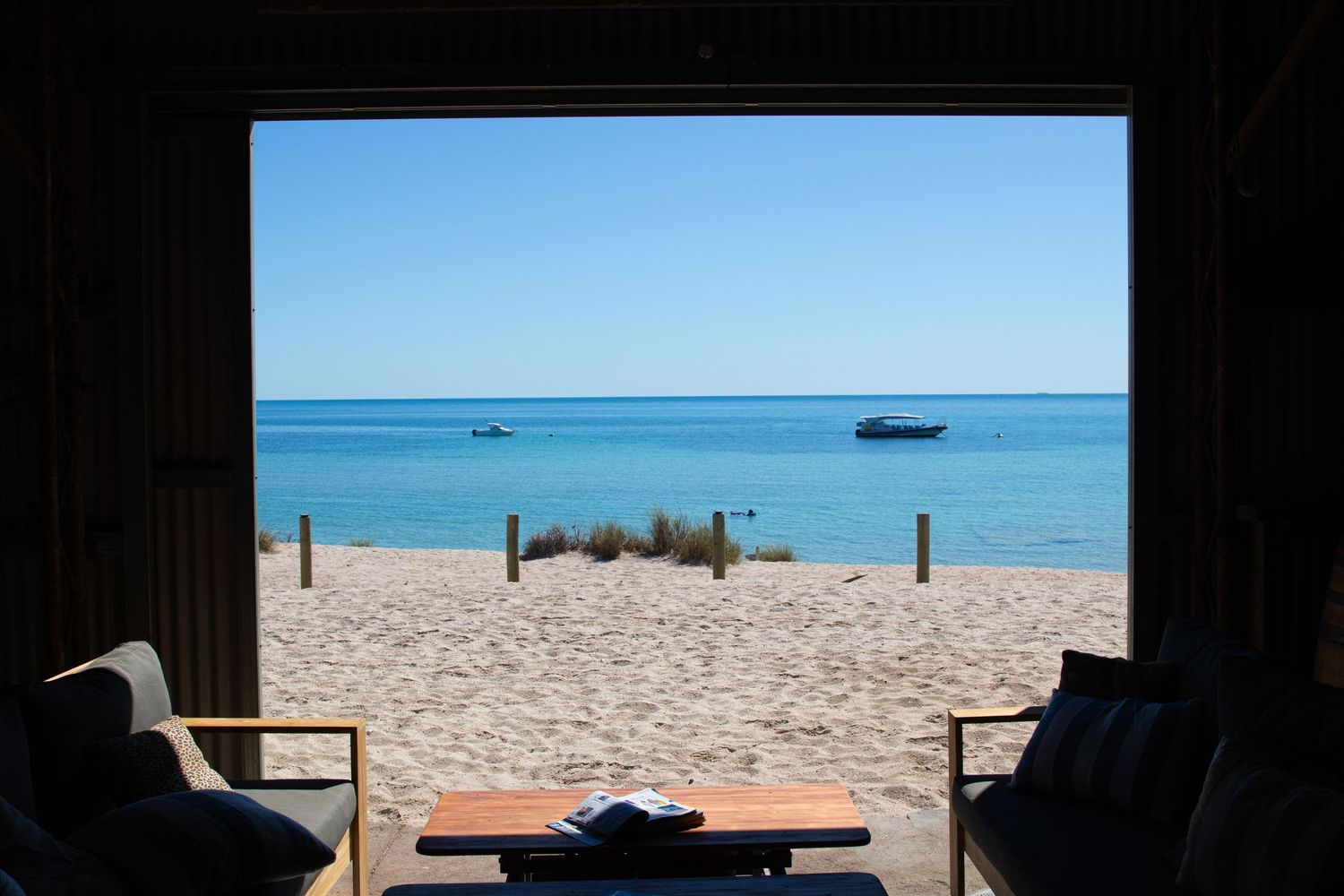 Stunning turquoise ocean view framed by open beach shack doorway with boats anchored at Dirk Hartog Island.