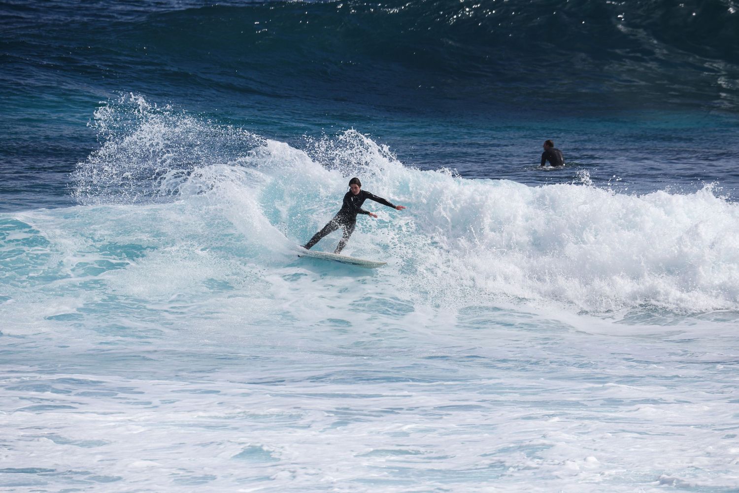 Two surfers navigating powerful white-capped waves in bright blue water.