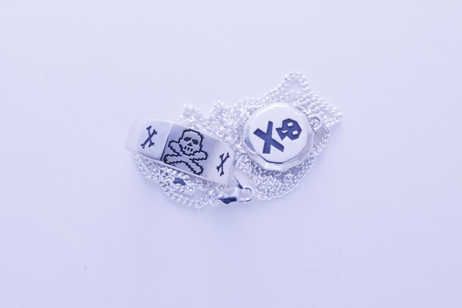 Close-up of silver skull and crossbones engraved charm pendants on chain.