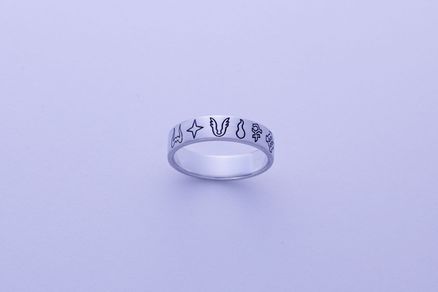 Silver band ring with engraved star, bunny, and floral symbols on a lavender background.