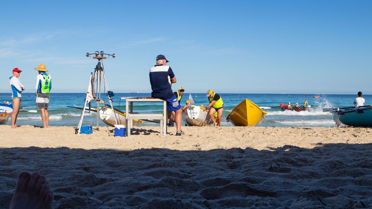Beach surf lifesaving competition with officials, equipment, and boats in the water.