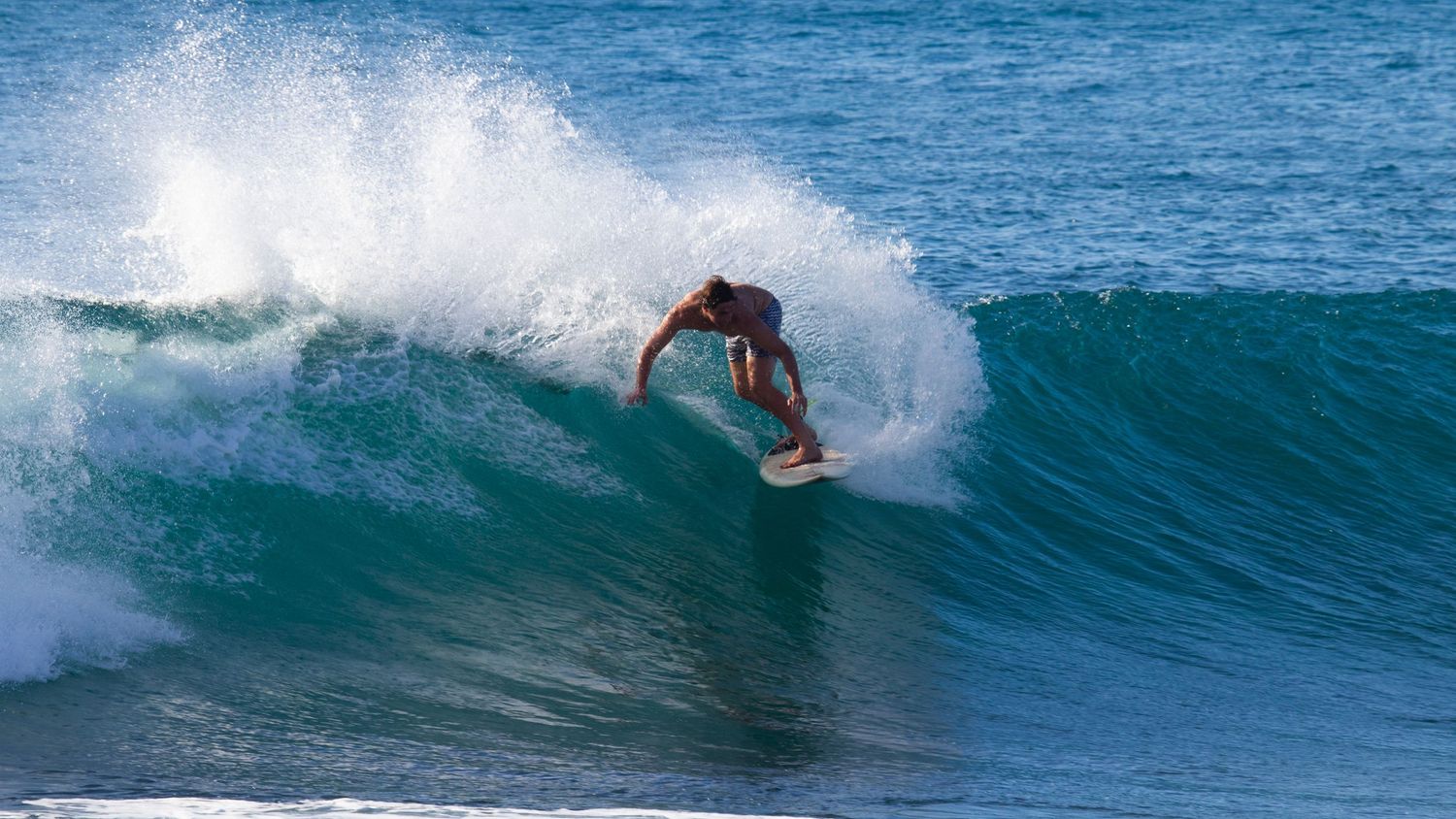 Surfer performing an aggressive top turn on a wave with turquoise water and white sea spray.