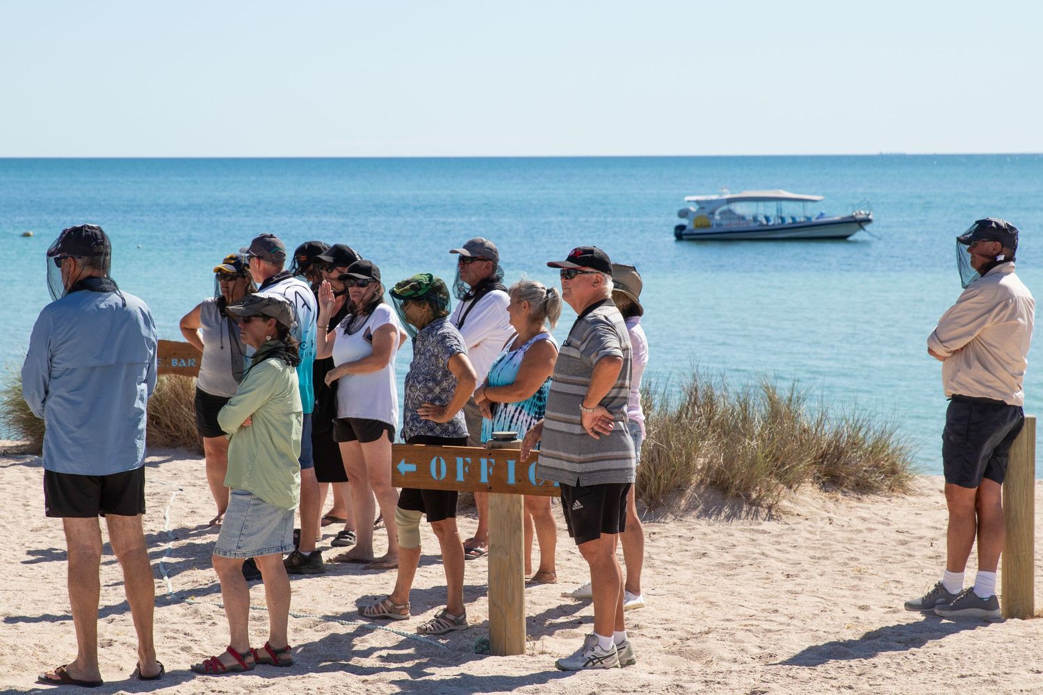 Group of tourists standing on sandy beach with turquoise ocean and boat in background, Dirk Hartog Island.