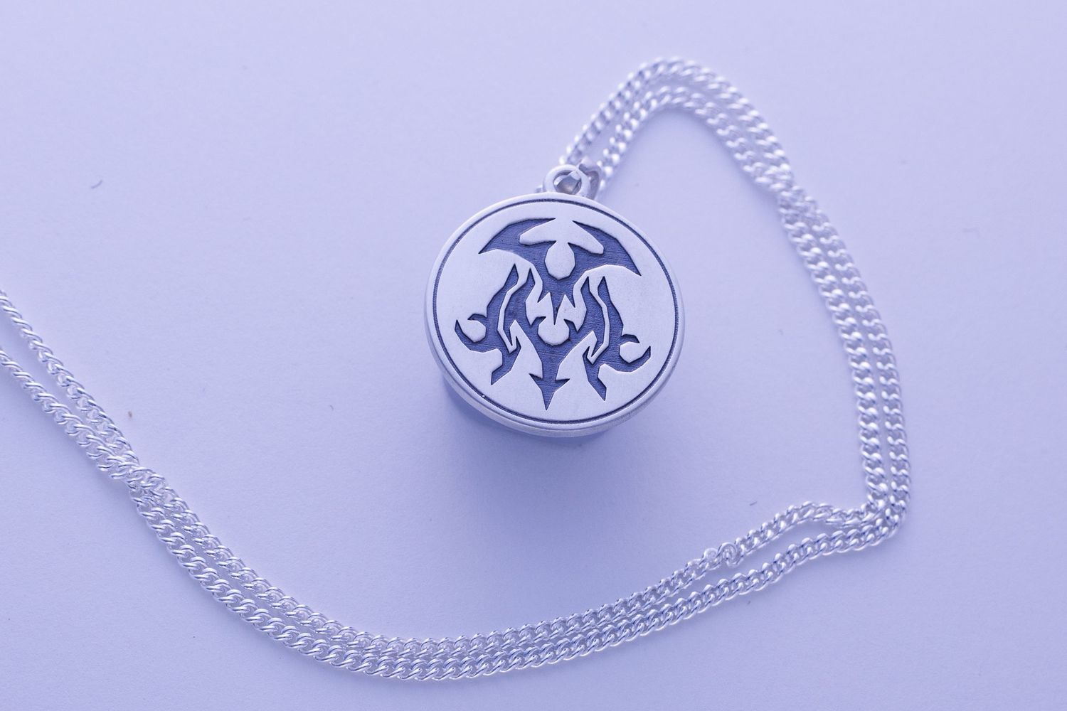 Silver round pendant necklace with tribal flame engraving on a lavender background.