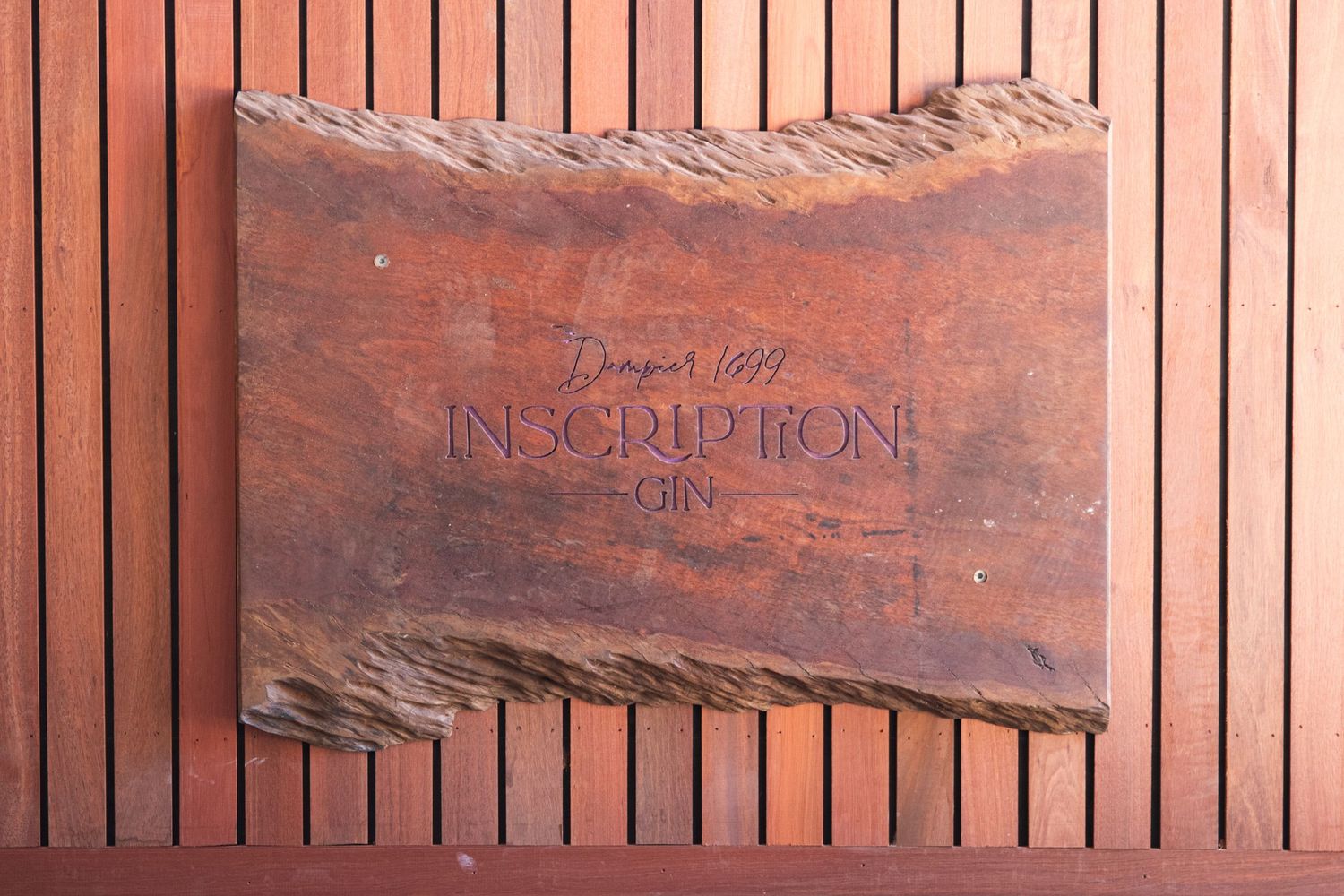 Inscription Gin wooden sign with rustic live edge detail mounted on a timber slatted wall.