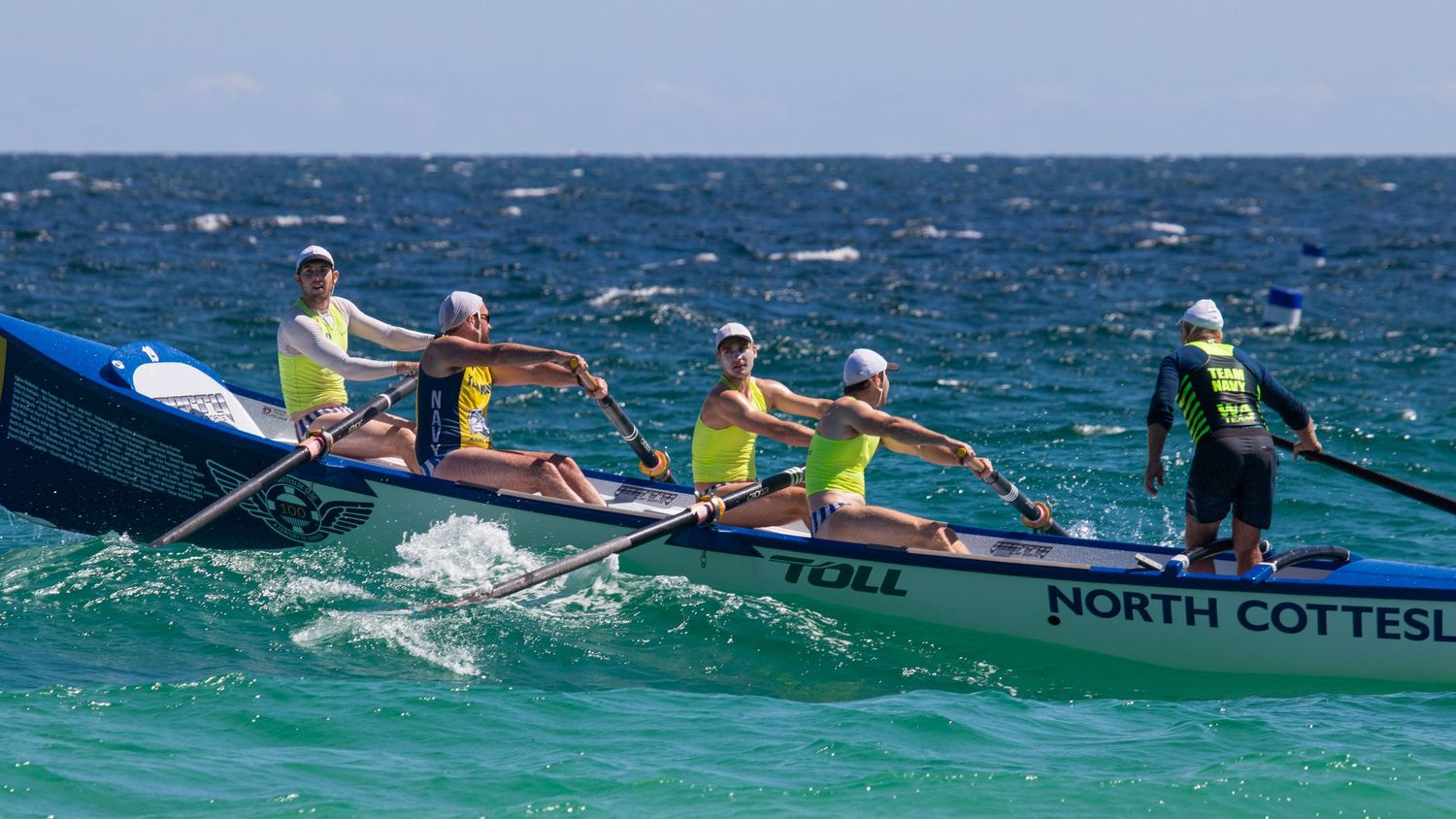 North Cottesloe four-person surf boat crew with sweep rowing through calm blue ocean waters.