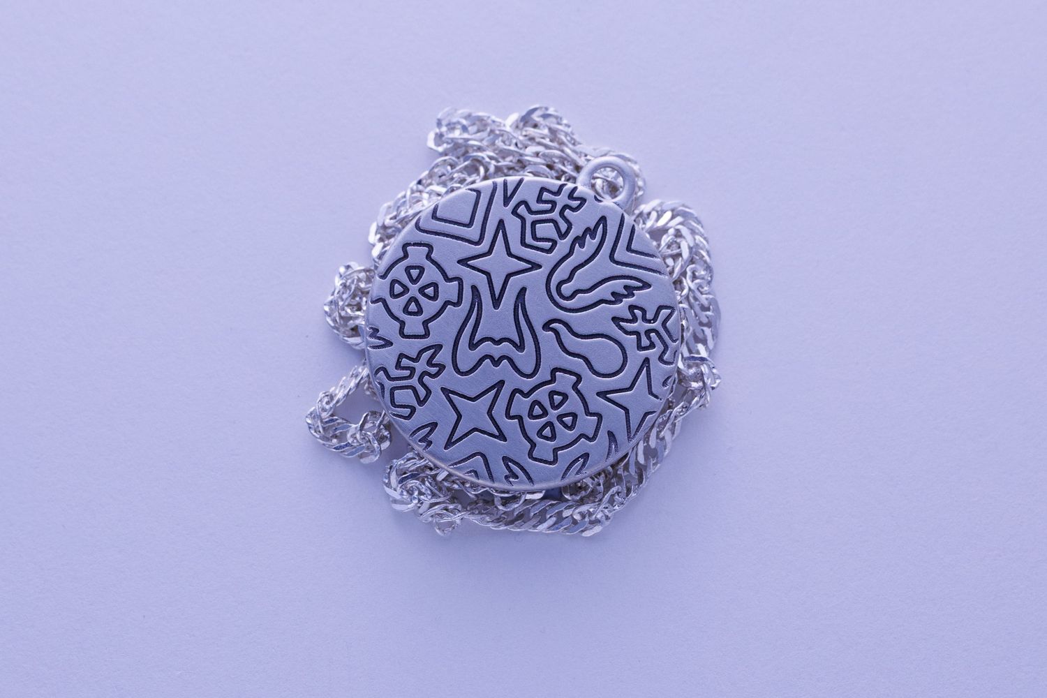Round silver pendant necklace with intricate engraved pattern featuring stars and abstract shapes on chain.