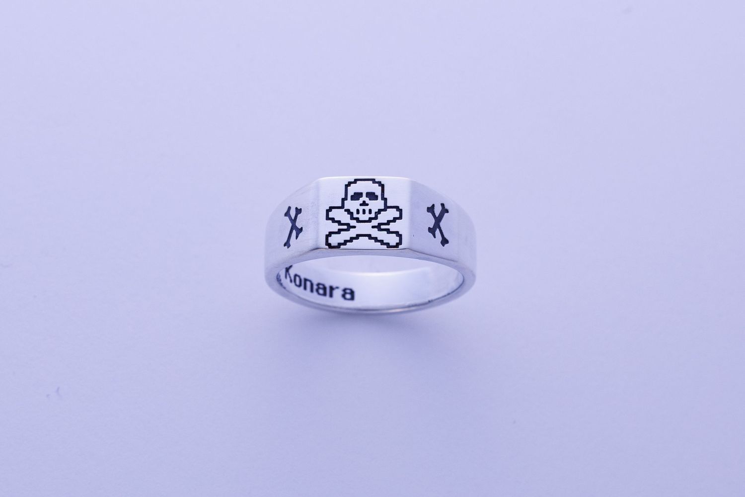 Silver Konara signet ring engraved with skull and crossbones design on a white background.