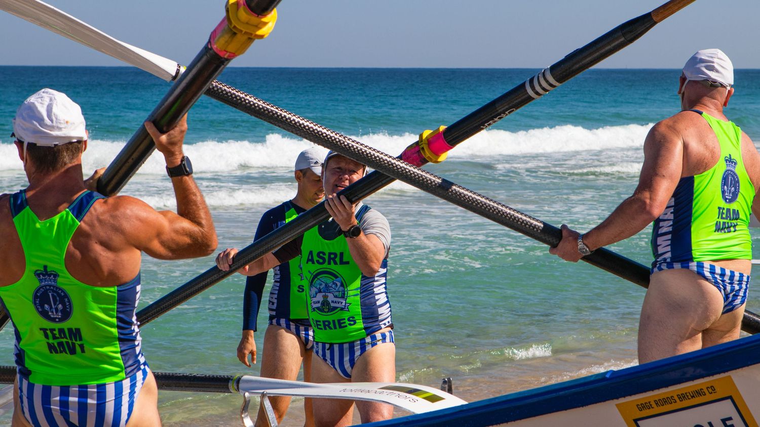 Surf boat crew members carry oars on a beach during an ASRL Series rowing competition in Australia.