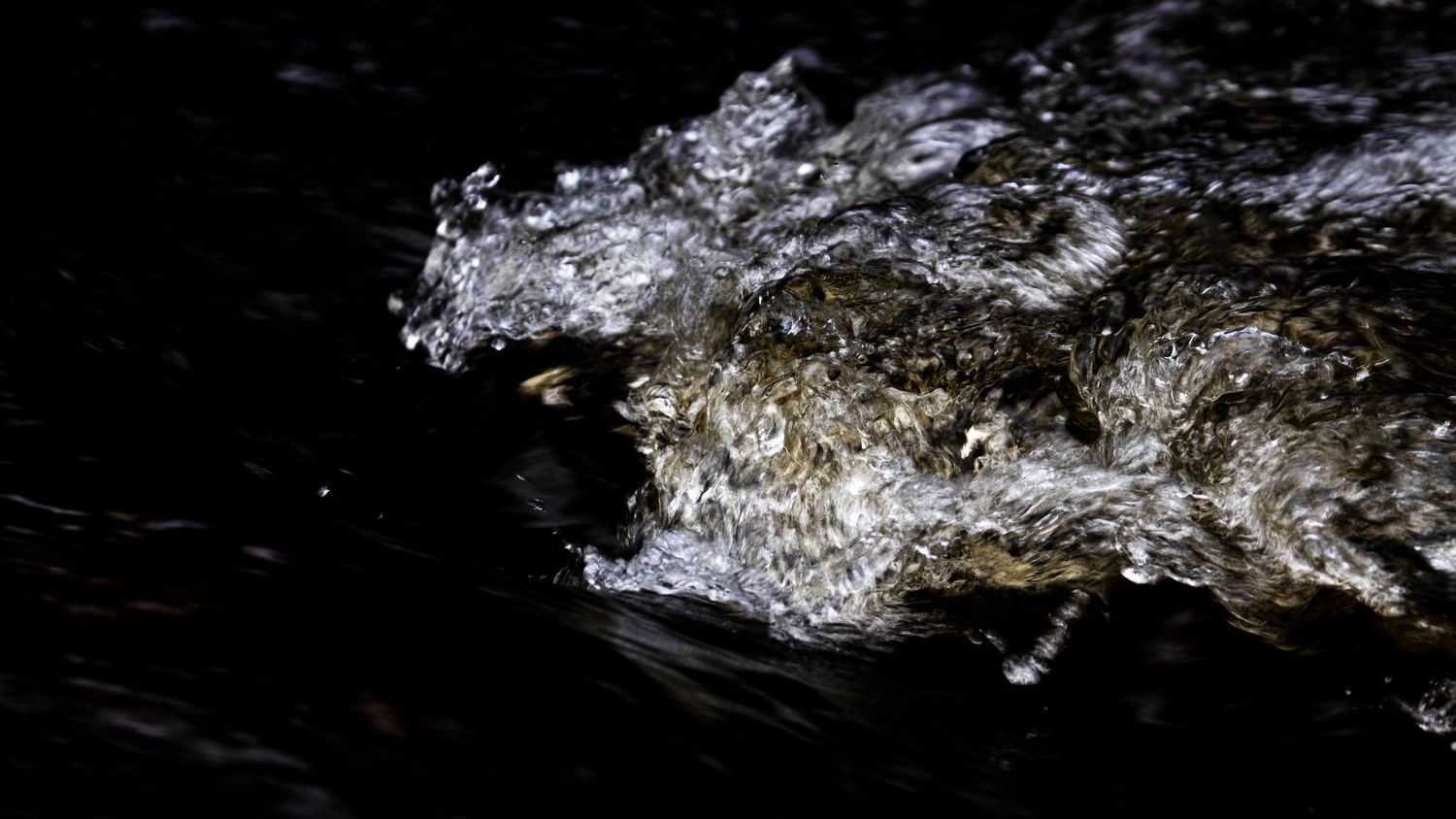 Turbulent white water splashing against dark rocks creating dramatic foam and spray patterns.