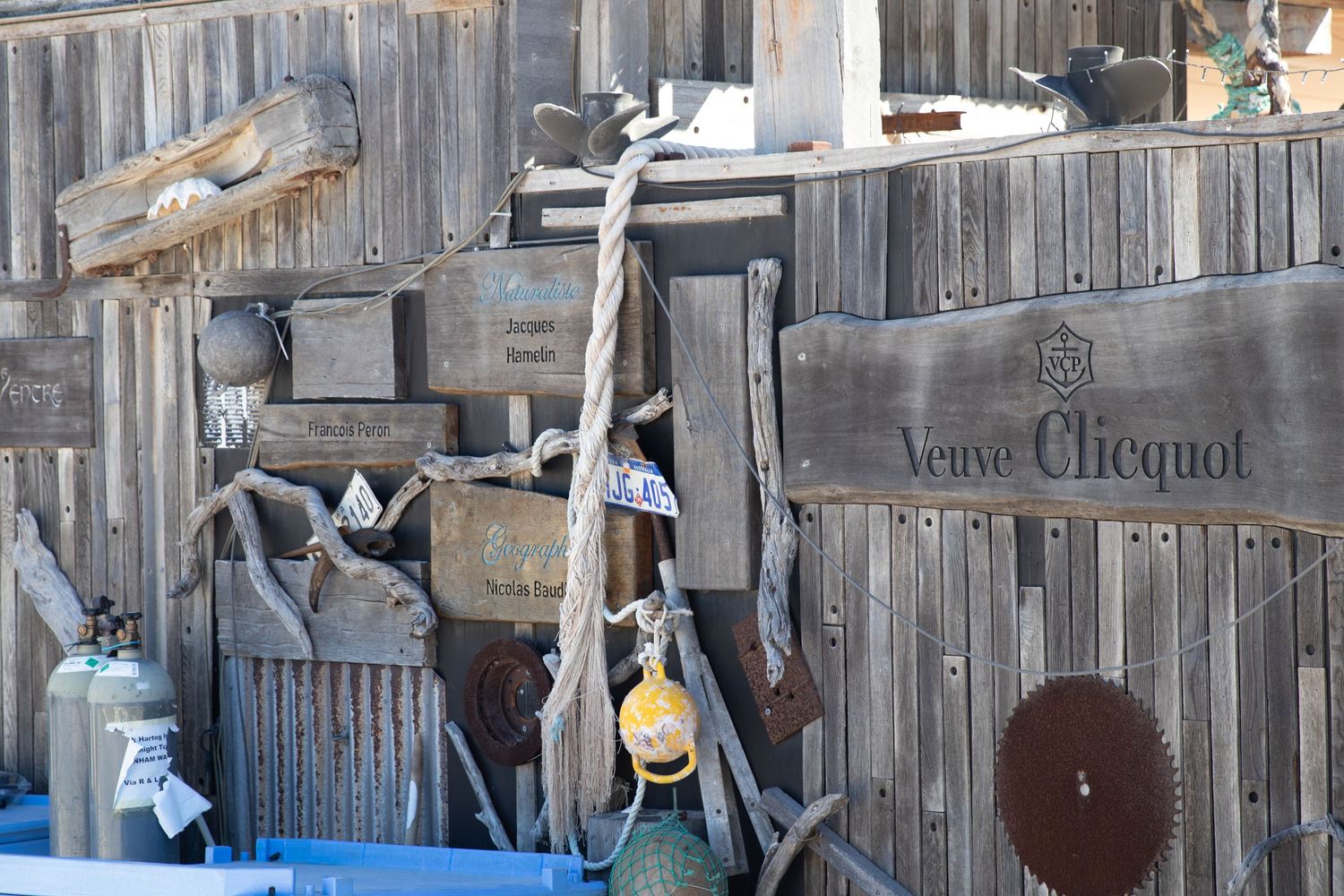 Weathered wooden wall display with vintage tools, rope and Veuve Clicquot signage at beach outstation.