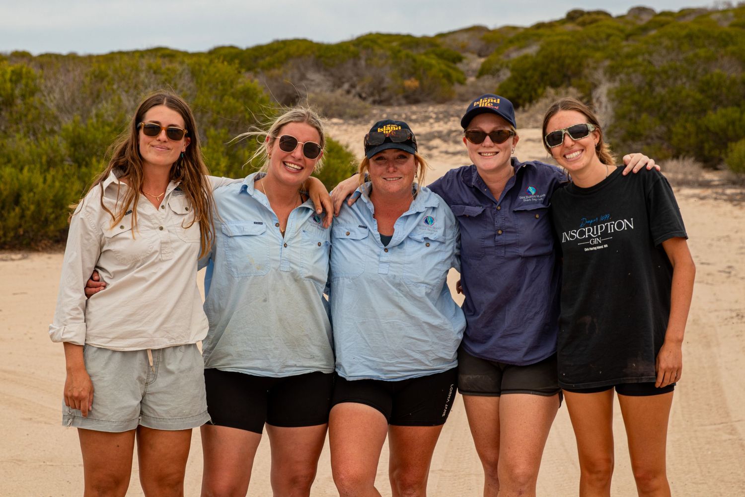 Five smiling women posing together on sandy beach trail at Dirk Hartog Island, Western Australia.