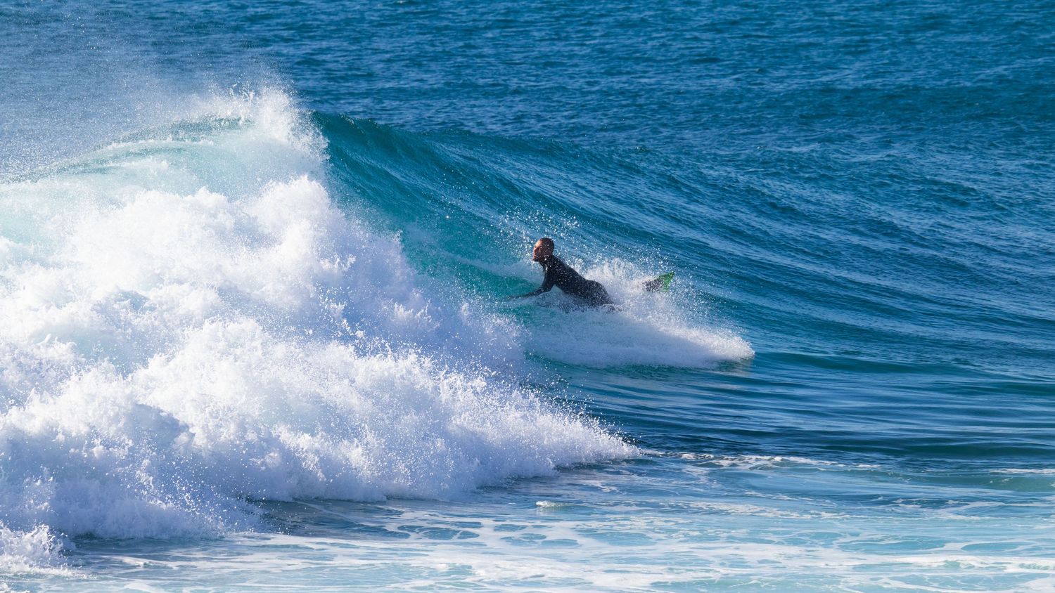 A surfer rides a powerful wave in the ocean, navigating through white water and turquoise swells.