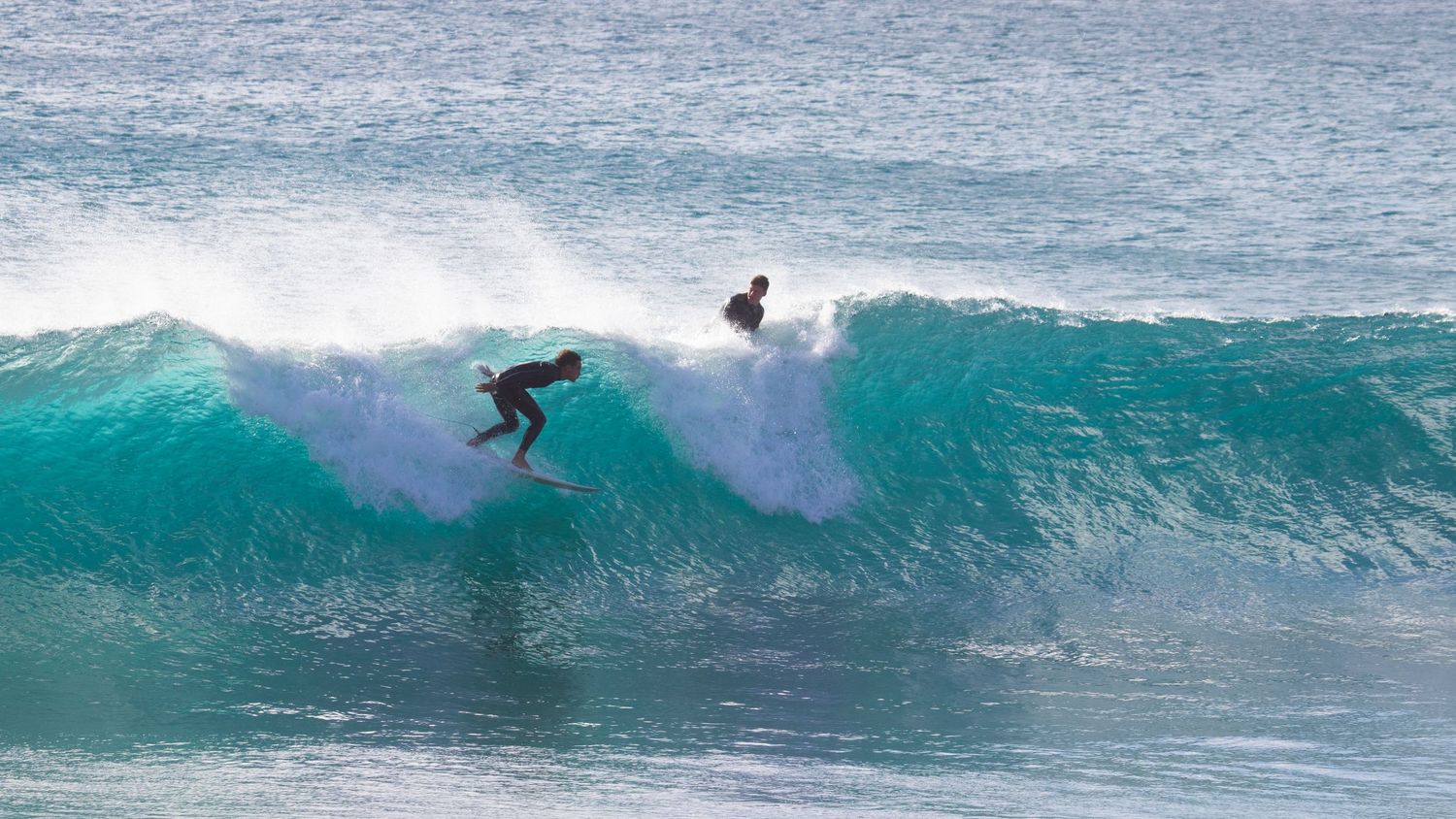 Two surfers riding a turquoise wave in the ocean.