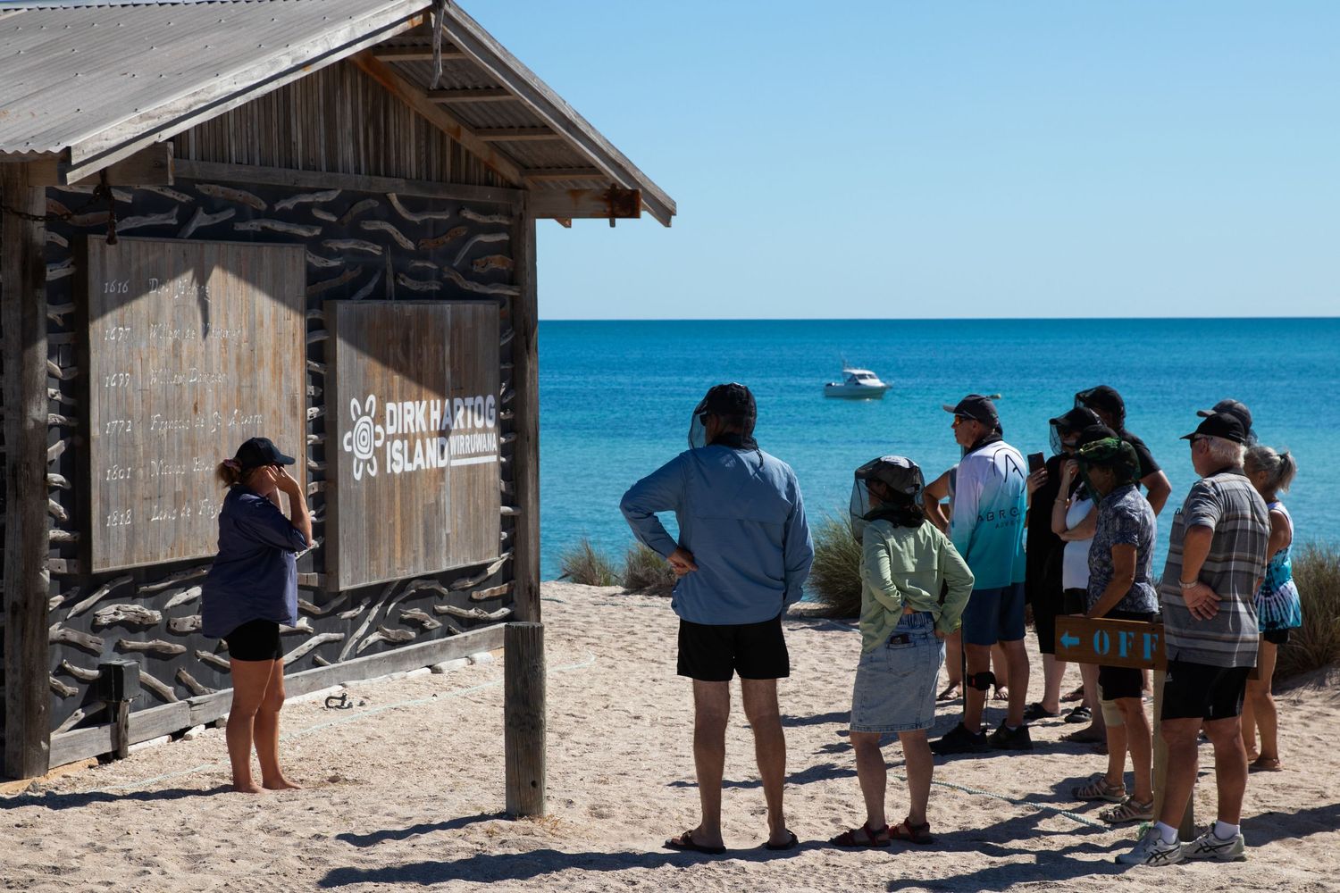 Tour guide presenting to group of tourists outside rustic wooden Dirk Hartog Island beach outstation.