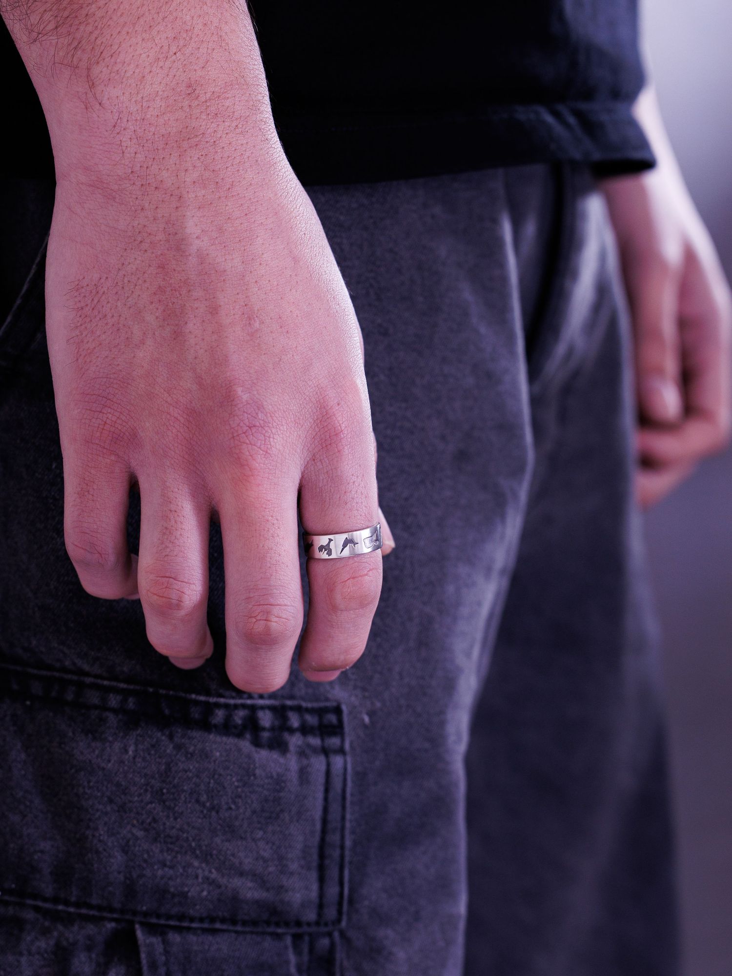 Close-up of a man's hand wearing a silver band ring with engraved lightning bolt design.